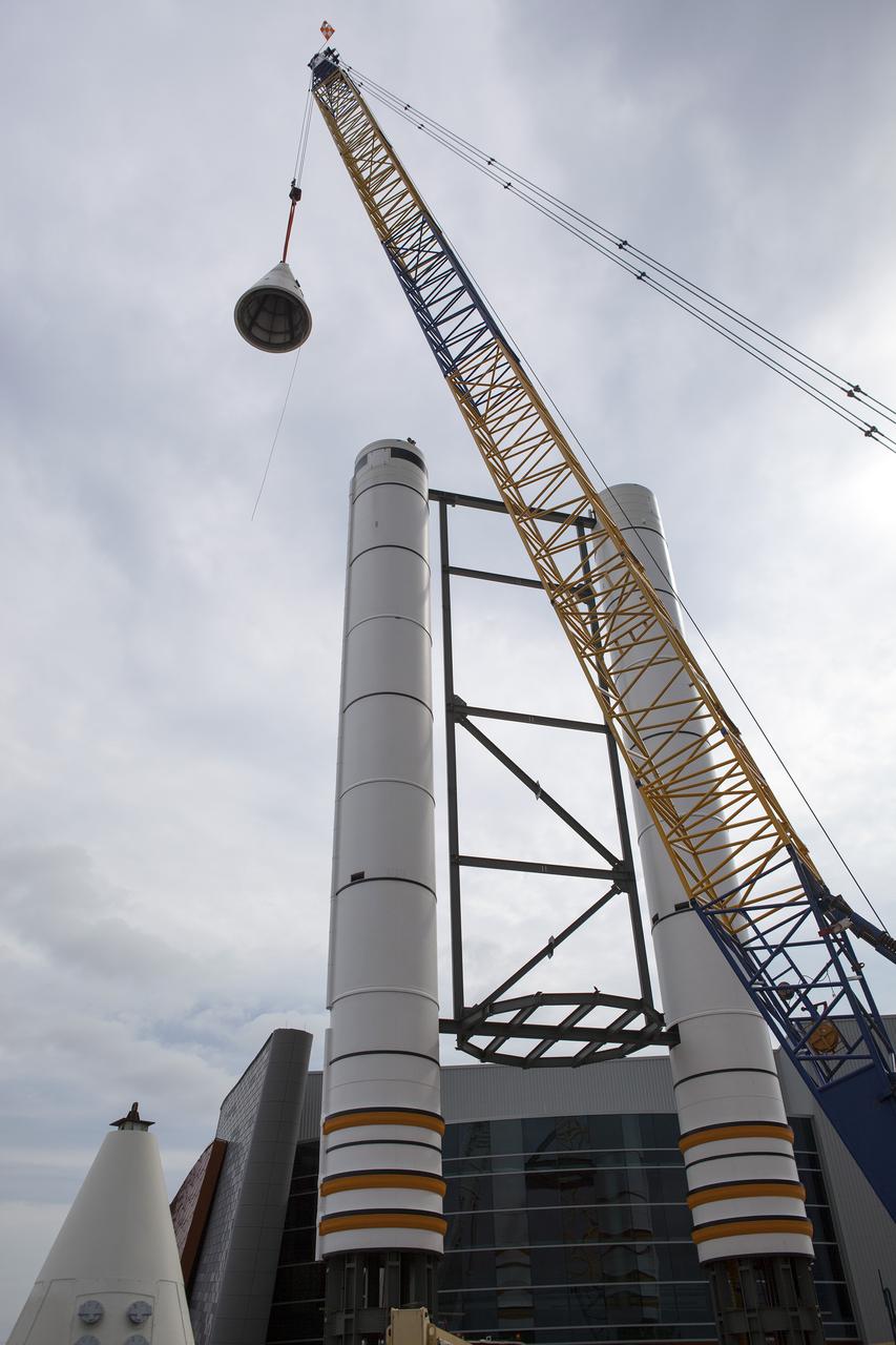 CAPE CANAVERAL, Fla. – A crane lifts a nose cone to top out one of a pair of replica space shuttle solid rocket boosters at the entry of the space shuttle Atlantis attraction under construction at the Kennedy Space Center Visitor Complex. Workers will use cranes to place the nose cones atop each of the model boosters. The building in the background houses the actual shuttle Atlantis. Photo credit: NASA_Dmitri Gerondidakis