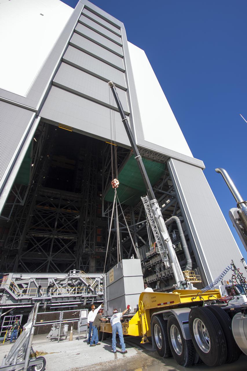 CAPE CANAVERAL, Fla. – In front of the Vehicle Assembly Building at NASA’s Kennedy Space Center in Florida, technicians monitor the progress as a large crane lowers a fuel tank from crawler-transporter 1 CT-1 in high bay 3 onto a flatbed truck. The fuel tank will be transported to the Wiltech facility at Kennedy for cleaning and inspection.  Work continues in high bay 3 to upgrade CT-1 as part of its general maintenance. CT-1 could be available to carry commercial launch vehicles to the launch pad. The crawler-transporters were used to carry the mobile launcher platform and space shuttle to Launch Complex 39 for space shuttle launches for 30 years.  Photo credit: NASA_Jim Grossman