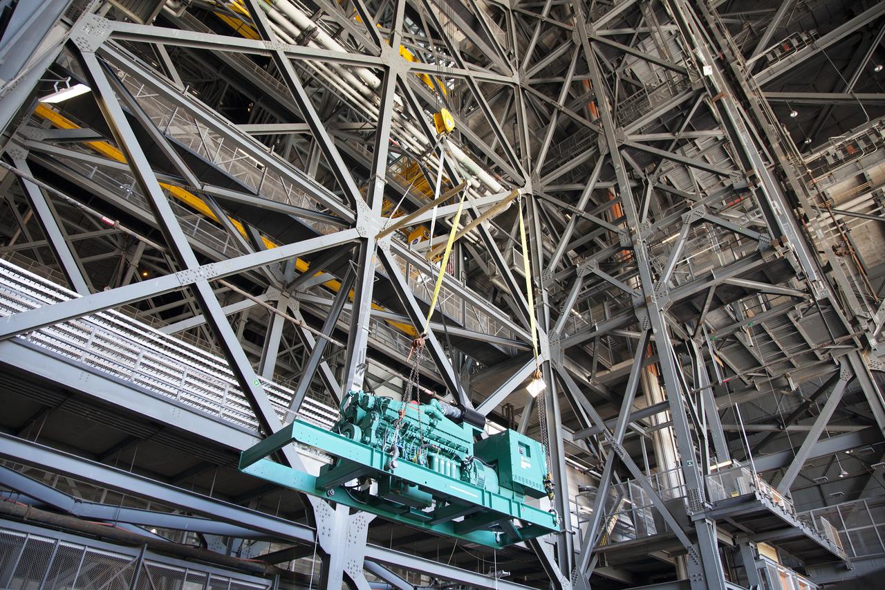 CAPE CANAVERAL, Fla. – Inside the Vehicle Assembly Building at NASA’s Kennedy Space Center in Florida, a large crane lifts a new generator up for installation in crawler-transporter 1, or CT-1.    Work continues in high bay 3 to upgrade CT-1 as part of its general maintenance. CT-1 could be available to carry commercial launch vehicles to the launch pad. The crawler-transporters were used to carry the mobile launcher platform and space shuttle to Launch Complex 39 for space shuttle launches for 30 years.  Photo credit: NASA_Daniel Casper