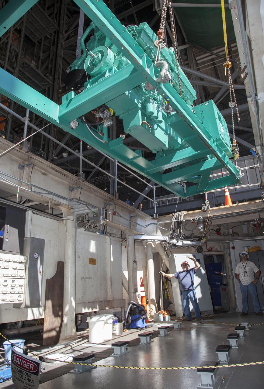CAPE CANAVERAL, Fla. – Inside the Vehicle Assembly Building at NASA’s Kennedy Space Center in Florida, technicians monitor the progress as a large crane lowers a new generator up for installation in crawler-transporter 1, or CT-1.    Work continues in high bay 3 to upgrade CT-1 as part of its general maintenance. CT-1 could be available to carry commercial launch vehicles to the launch pad. The crawler-transporters were used to carry the mobile launcher platform and space shuttle to Launch Complex 39 for space shuttle launches for 30 years.  Photo credit: NASA_Daniel Casper