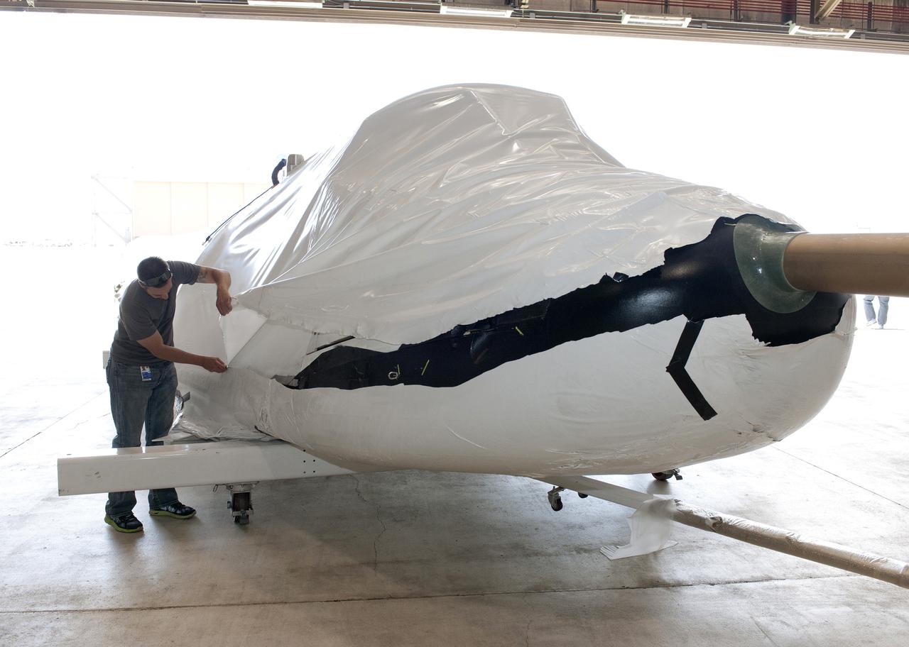 Edwards, Calif. – ED-0144-03 - Plastic wrapping that protected the Sierra Nevada Corporation, or SNC, Dream Chaser flight test vehicle during its transport from Colorado is carefully removed by SNC employee Jason Dixon following the craft's arrival at NASA's Dryden Flight Research Center in southern California. The prototype space access vehicle will undergo ground and approach-and-landing flight tests in the coming months at Dryden as part of NASA's Commercial Crew Program, or CCP, development work. SNC is one of three companies working with CCP during the agency's Commercial Crew Integrated Capability, or CCiCap, initiative, which is intended to lead to the availability of commercial human spaceflight services for government and commercial customers. To learn more about CCP and its industry partners, visit www.nasa.gov_commercialcrew. Image credit: NASA_Tom Tschida