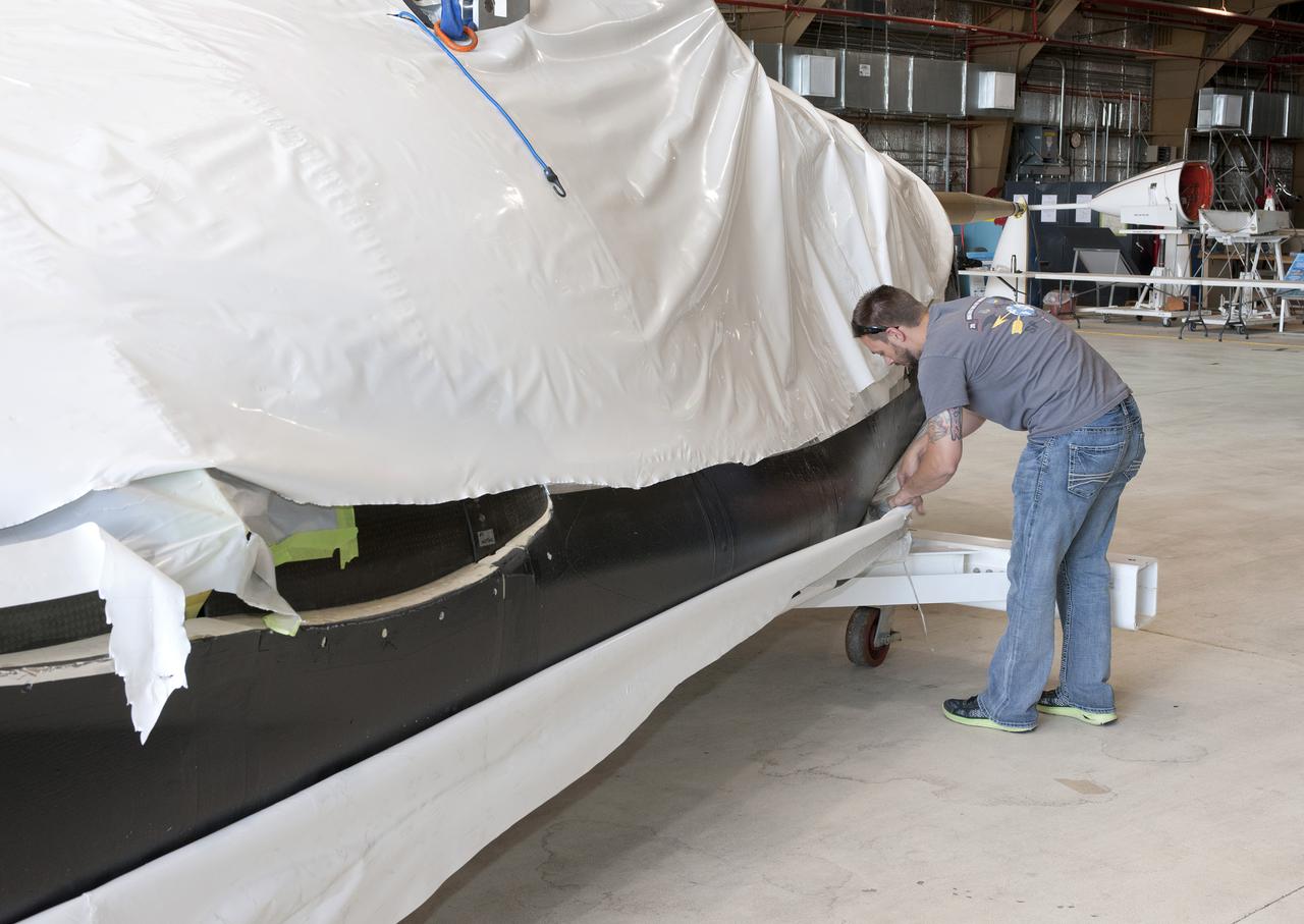 Edwards, Calif. – ED-0144-05 - Plastic wrapping that protected the Sierra Nevada Corporation, or SNC, Dream Chaser flight test vehicle during its transport from Colorado is carefully removed by SNC employee Jason Dixon following the craft's arrival at NASA's Dryden Flight Research Center in southern California. The prototype space access vehicle will undergo ground and approach-and-landing flight tests in the coming months at Dryden as part of NASA's Commercial Crew Program, or CCP, development work.    SNC is one of three companies working with CCP during the agency's Commercial Crew Integrated Capability, or CCiCap, initiative, which is intended to lead to the availability of commercial human spaceflight services for government and commercial customers. To learn more about CCP and its industry partners, visit www.nasa.gov_commercialcrew. Image credit: NASA_Tom Tschida