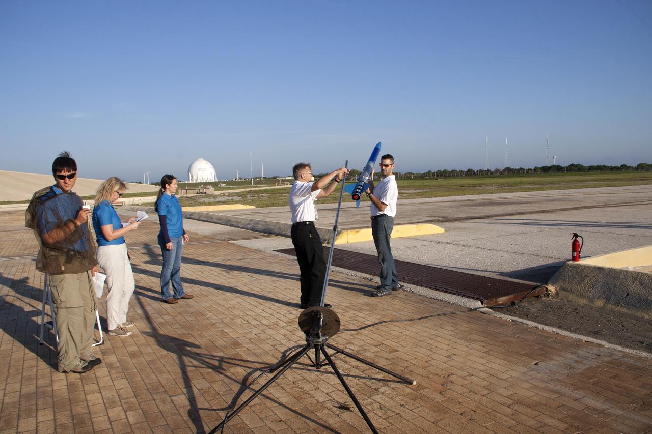 CAPE CANAVERAL, Fla. -- At NASA's Kennedy Space Center in Florida, as Morgan Simpson of Flight Hardware Processing, Susan Danley of Flight Structures and Kim Simpson of Fluids, Mechanical and Structural Systems look on, Gary Dahlke of Engineering and Technology, left, and Leandro James of Systems Hardware Engineering attach a small rocket prior to its launch stand as part of Rocket University. The goal was to test its systems and to verify that it performed as designed. As part of Rocket University, the engineers are given an opportunity to work a fast-track project to develop skills in developing spacecraft systems of the future. As NASA plans for future spaceflight programs to low-Earth orbit and beyond, teams of engineers at Kennedy are gaining experience in designing and flying launch vehicle systems on a small scale. Four teams of five to eight members from Kennedy are designing rockets complete with avionics and recovery systems. Launch operations require coordination with federal agencies, just as they would with rockets launched in support of a NASA mission. Photo credit: NASA_Jim Grossmann