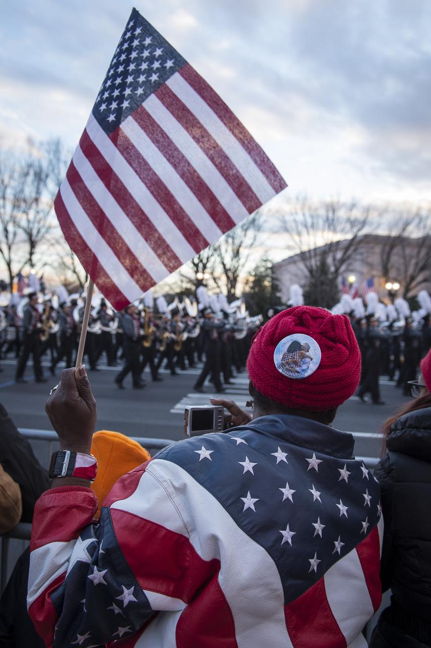 A parade-goer holds dressed in a Stars and Stripes coat waves a flag while watching the 2013 Inaugural Parade honoring President Barack Obama, Monday, Jan. 21, 2013, along Pennsylvania Avenue in Washington. Photo Credit : (NASA/Paul E. Alers)
