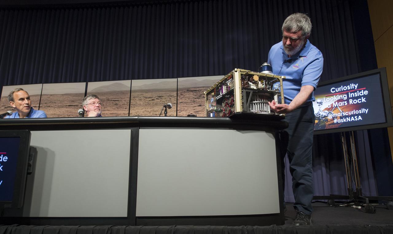 Paul Mahaffy (right), principal investigator for Curiosity's Sample Analysis at Mars (SAM) investigation at NASA's Goddard Space Flight Center in Maryland, demonstrates how the SAM instrument drilled and captured rock samples on the surface of Mars at a news conference, Tuesday, March 12, 2013 at NASA Headquarters in Washington.  The analysis of the rock sample collected shows ancient Mars could have supported living microbes.  Photo Credit:  (NASA/Carla Cioffi)