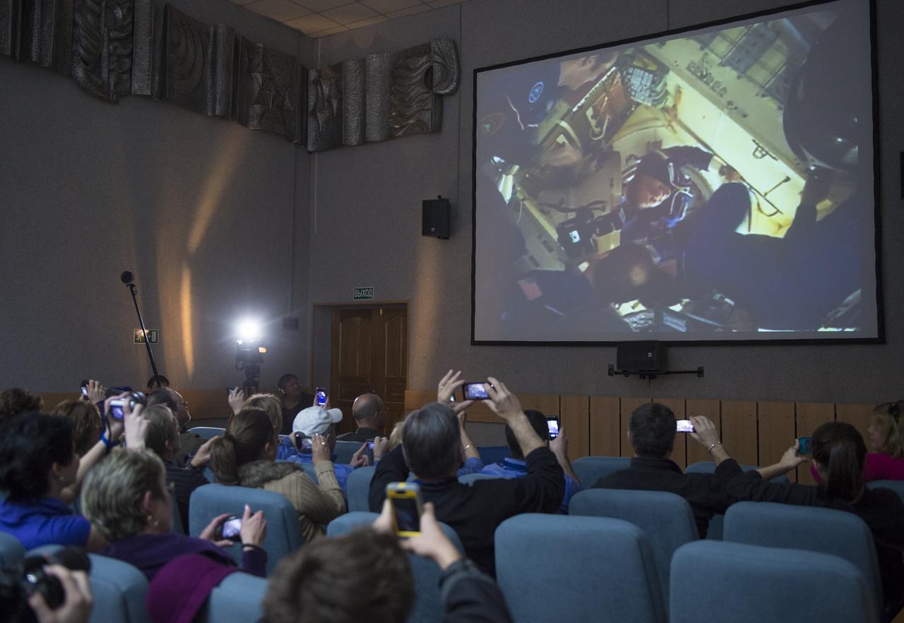 Guests watch video of Expedition 35 Soyuz Commander Pavel Vinogradov entering the International Space Station after docking the Soyuz TMA-08M to the station following its first ever expedited trip to the orbiting complex, Friday, March 29, 2013, at the Cosmonaut Hotel in Baikonur, Kazakhstan.  The Soyuz reached the station in less than six hours and after only four orbits, instead of its usual two-day route.  Photo Credit:  (NASA/Carla Cioffi)