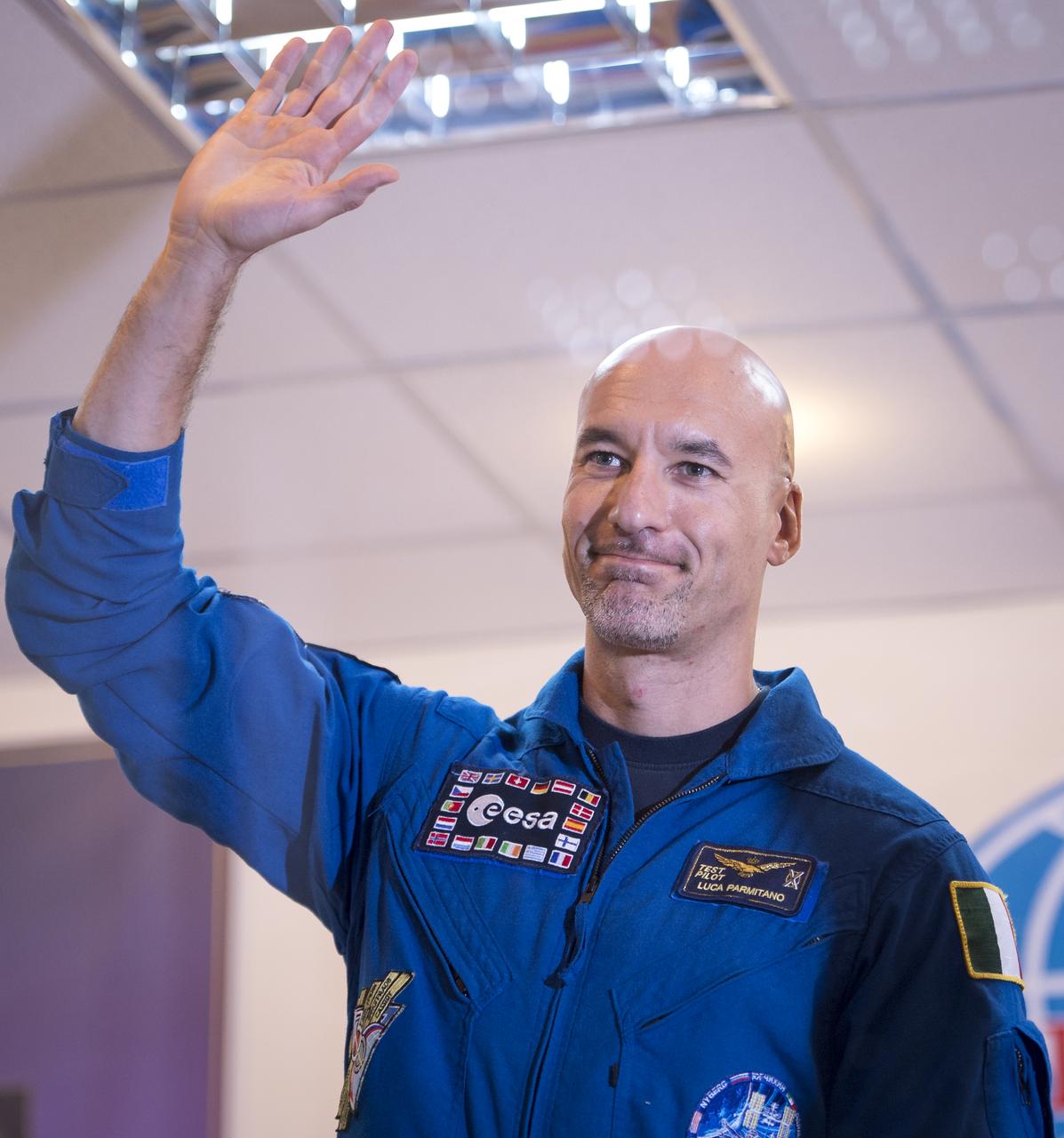 Expedition 36/37 Flight Engineer Luca Parmitano of the European Space Agency waves during the crew press conference at the Cosmonaut Hotel, Monday, May 27, 2013, in Kazakhstan. Parmitano and his fellow crew members, Soyuz Commander Fyodor Yurchikhin of the Russian Federal Space Agency (Roscosmos), and Flight Engineer Karen Nyberg of NASA, were in quarantine and kept behind glass during the press conference in preparation for their launch on a Soyuz rocket to the International Space Station (ISS) on Wednesday May 29, Kazakh time. Photo credit: (NASA/Bill Ingalls)