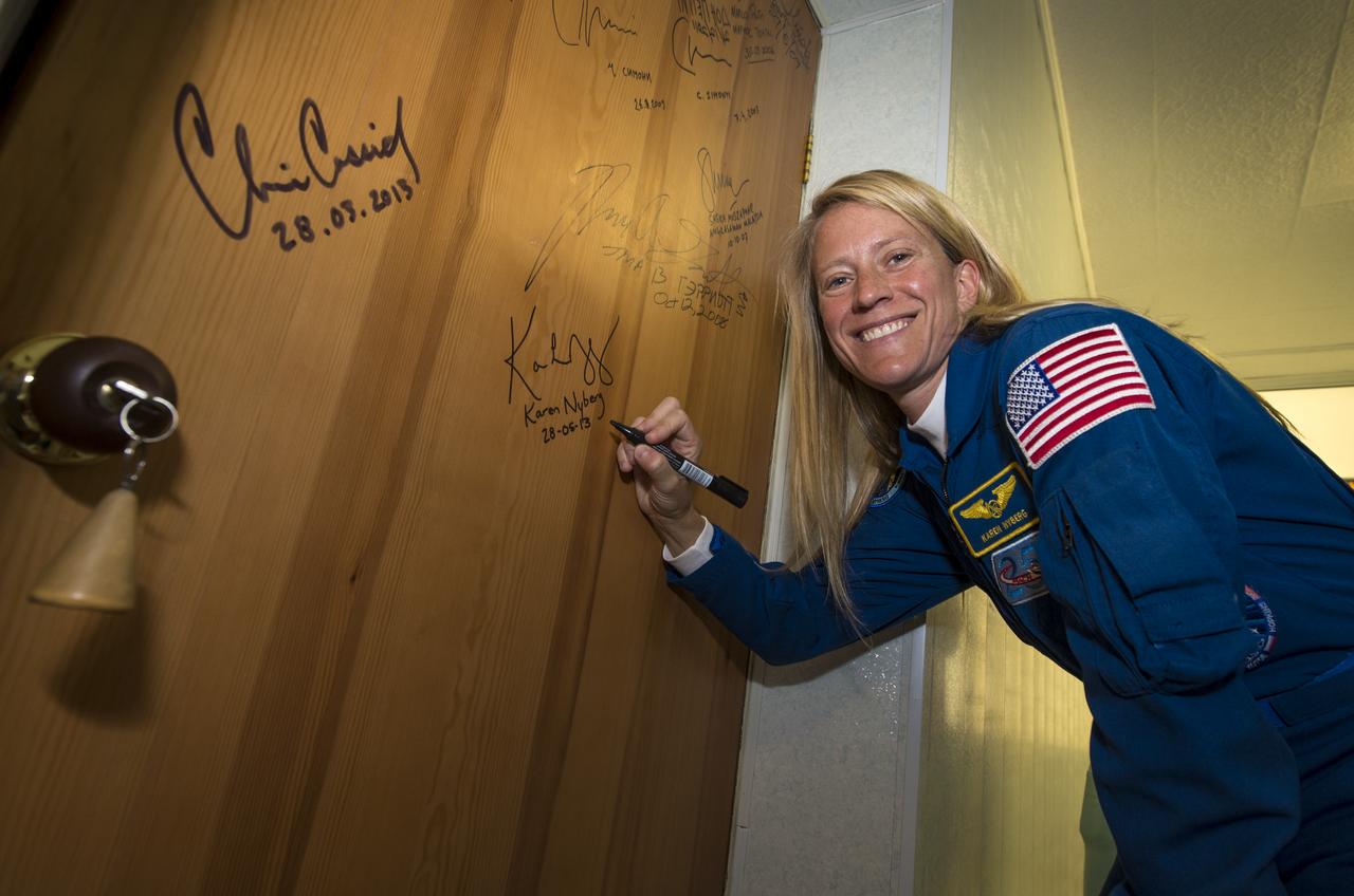 Expedition 36/37  Flight Engineer Karen Nyberg of NASA pauses for a photo while signing a hotel room door at the Cosmonaut Hotel, Tuesday, May 28, 2013, in Baikonur, Kazakhstan. Nyberg and her fellow crew members, Soyuz Commander Fyodor Yurchikhin of the Russian Federal Space Agency (Roscosmos), and, Flight Engineer, and Luca Parmitano of the European Space Agency, were departing the hotel in preparation for their launch on a Soyuz rocket to the International Space Station (ISS) on Wednesday May 29, Kazakh time. Photo credit: (NASA/Bill Ingalls)