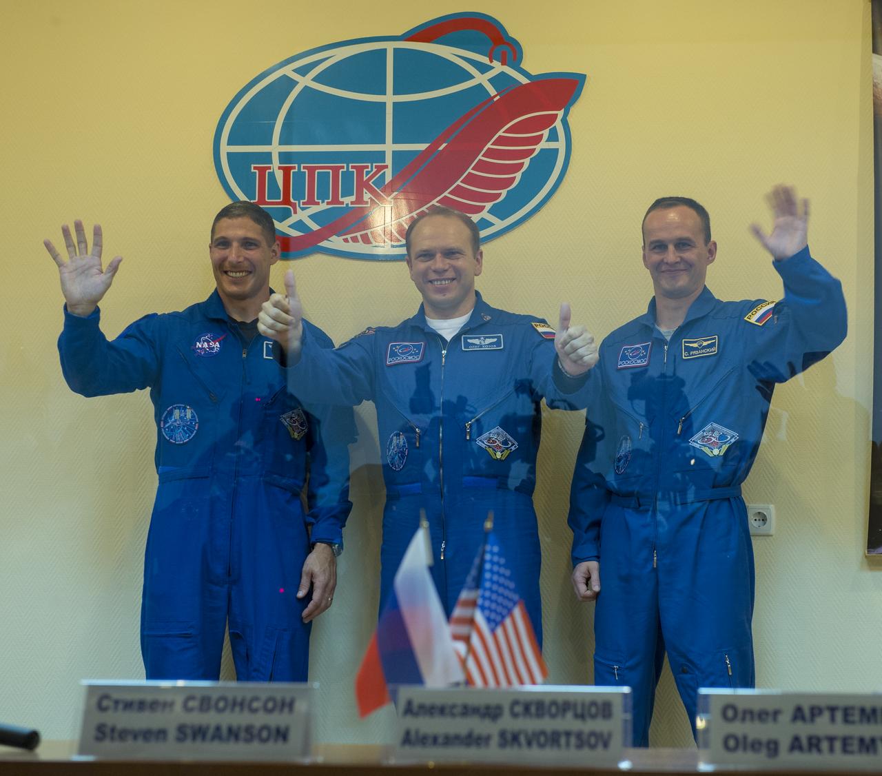 Expedition 37 NASA Flight Engineer Michael Hopkins, far left, Soyuz Commander Oleg Kotov and Russian Flight Engineer Sergey Ryazanskiy, far right, wave and give the thumbs up following a press conference held at the Cosmonaut Hotel, on Tuesday, Sept. 24, 2013, in Baikonur, Kazakhstan. Launch of the Soyuz rocket is scheduled for September 26 and will send Hopkings, Kotov, Ryazanski on a five and a half-month mission aboard the International Space Station.  Photo Credit: (NASA/Carla Cioffi)