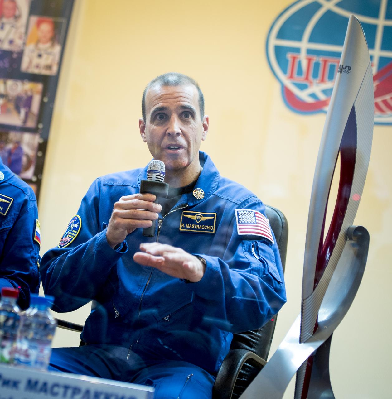 Expedition 38 Flight Engineer Rick Mastracchio of NASA talks, while in quarantine behind glass, during the final press conference held a day ahead of his launch with fellow crew mates, Soyuz Commander Mikhail Tyurin of Roscosmos, and, Flight Engineer Koichi Wakata of the Japan Aerospace Exploration Agency, to the International Space Station, Wednesday, Nov. 6, 2013 at the Cosmonaut Hotel in Baikonur, Kazakhstan. An Olympic torch that will be launched with the crew for a four-day visit to the station is seen next to Mastracchio. The torch will return to Earth with another trio of station residents on Nov. 11 and will be part of the torch relay that ends with the lighting of the flame at the Fisht Stadium in Sochi, Russia Feb. 7 to mark the opening of the 2014 Winter Olympics. Photo Credit: (NASA/Bill Ingalls)