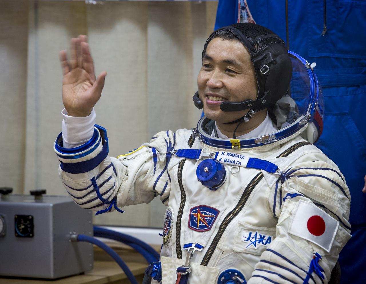 Expedition 38 Flight Engineer Koichi Wakata of the Japan Aerospace Exploration Agency waves hello to family members gathered to watch him through glass as he and fellow crew mates, Soyuz Commander Mikhail Tyurin of Roscosmos, and, Flight Engineer Rick Mastracchio of NASA, have their Russian Sokol suits pressure checked a few hours ahead of their launch, Thursday, Nov. 7, 2013, in Baikonur, Kazakhstan. Tyurin, Wakata, and, Mastracchio will launch in their Soyuz TMA-11M spacecraft to the International Space Station to begin a six-month mission. Photo Credit (NASA/Bill Ingalls)