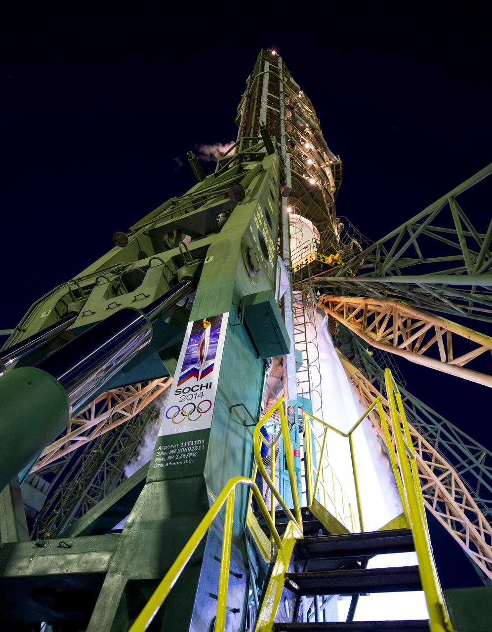 A sign for the Sochi 2014 Winter Olympics is seen at the base of the Soyuz launch gantry after Expedition 38 Soyuz Commander Mikhail Tyurin of Roscosmos, Flight Engineer Koichi Wakata of the Japan Aerospace Exploration Agency, and, Flight Engineer Rick Mastracchio of NASA, boarded their soyuz TMA-11M rocket for their launch to the International Space Station, Thursday, Nov. 7, 2013, in Baikonur, Kazakhstan. The rocket is adorned with the logo of the Sochi Olympic Organizing Committee and other related artwork to commemorate the launch of the Olympic torch with the crew for a four-day visit to the station. The torch will return to Earth with another trio of station residents on Nov. 11 and will be part of the torch relay that ends with the lighting of the flame at the Fisht Stadium in Sochi, Russia Feb. 7 to mark the opening of the 2014 Winter Olympics. Photo Credit (NASA/Bill Ingalls)
