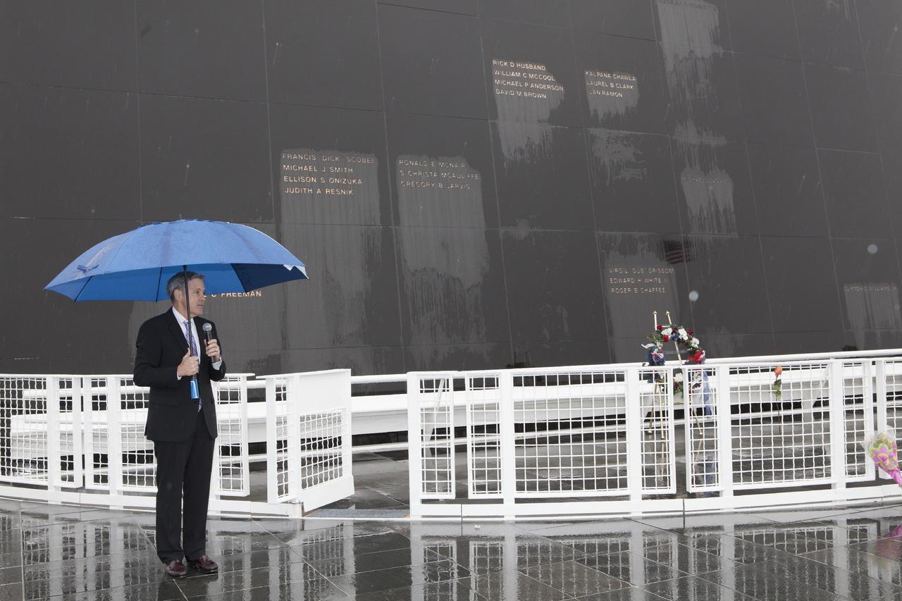 CAPE CANAVERAL, Fla. -- Under rainy skies, Kennedy Space Center Director Bob Cabana speaks to guests after placing a wreath in front of the Space Mirror Memorial at the spaceport's Visitor Complex during NASA's Day of Remembrance. The brief ceremony honored the astronauts of Apollo 1, who were lost in 1967, the shuttle Challenger crew, who perished in 1986, the space shuttle Columbia astronauts who were lost in 2003, as well as other astronauts who gave their lives while furthering the cause of exploration and discovery.    Dedicated in 1991, the names of fallen astronauts are emblazoned the monument's 4.5-foot-high-by-50-foot-wide polished black granite surface which reflects the sky and has been designated by Congress as a National Memorial. Photo credit: NASA/Dimitri Gerondidakis
