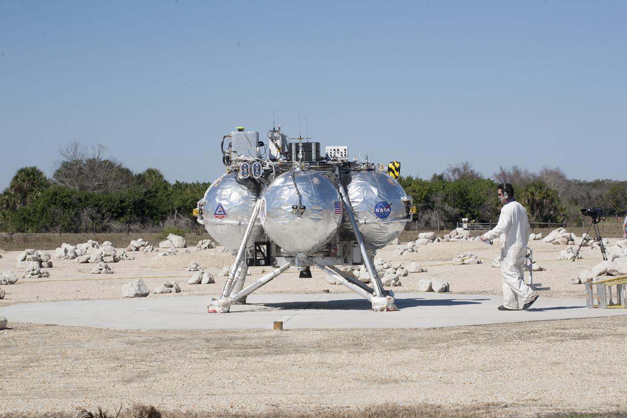 CAPE CANAVERAL, Fla. – A technicians checks the Project Morpheus prototype lander after it lands on a dedicated pad inside the autonomous landing and hazard avoidance technology, or ALHAT, hazard field at the north end of the Shuttle Landing Facility at NASA’s Kennedy Space Center in Florida. Morpheus launched from the ground over a flame trench on its fifth free flight test at around 1 p.m. EST. It ascended 467 feet, more than 160 feet higher than its last test. Morpheus flew forward, covering 637 feet in 30 seconds before descending on target. Project Morpheus tests NASA’s ALHAT and an engine that runs on liquid oxygen and methane, or green propellants, into a fully-operational lander that could deliver cargo to other planetary surfaces.  The landing facility provides the lander with the kind of field necessary for realistic testing, complete with rocks, craters and hazards to avoid. Morpheus’ ALHAT payload will allow it to navigate to clear landing sites amidst rocks, craters and other hazards during its descent. Project Morpheus is being managed under the Advanced Exploration Systems, or AES, Division in NASA’s Human Exploration and Operations Mission Directorate. The efforts in AES pioneer new approaches for rapidly developing prototype systems, demonstrating key capabilities and validating operational concepts for future human missions beyond Earth orbit. For more information, visit http:__morpheuslander.jsc.nasa.gov. Photo credit: NASA_Kim Shiflett