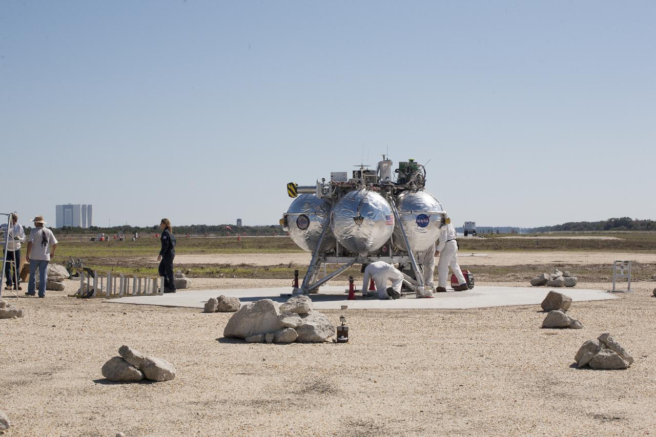 CAPE CANAVERAL, Fla. – Technicians and engineers check the Project Morpheus prototype lander after it lands on a dedicated pad inside the autonomous landing and hazard avoidance technology, or ALHAT, hazard field at the north end of the Shuttle Landing Facility at NASA’s Kennedy Space Center in Florida. Morpheus launched from the ground over a flame trench on its fifth free flight test at around 1 p.m. EST. It ascended 467 feet, more than 160 feet higher than its last test. Morpheus flew forward, covering 637 feet in 30 seconds before descending on target. Project Morpheus tests NASA’s ALHAT and an engine that runs on liquid oxygen and methane, or green propellants, into a fully-operational lander that could deliver cargo to other planetary surfaces.  The landing facility provides the lander with the kind of field necessary for realistic testing, complete with rocks, craters and hazards to avoid. Morpheus’ ALHAT payload will allow it to navigate to clear landing sites amidst rocks, craters and other hazards during its descent. Project Morpheus is being managed under the Advanced Exploration Systems, or AES, Division in NASA’s Human Exploration and Operations Mission Directorate. The efforts in AES pioneer new approaches for rapidly developing prototype systems, demonstrating key capabilities and validating operational concepts for future human missions beyond Earth orbit. For more information, visit http:__morpheuslander.jsc.nasa.gov. Photo credit: NASA_Kim Shiflett
