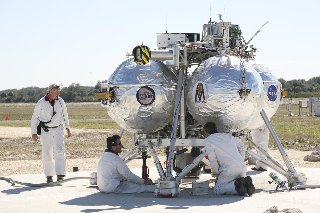CAPE CANAVERAL, Fla. – Technicians and engineers check the Project Morpheus prototype lander after it lands on a dedicated pad inside the autonomous landing and hazard avoidance technology, or ALHAT, hazard field at the north end of the Shuttle Landing Facility at NASA’s Kennedy Space Center in Florida. Morpheus launched from the ground over a flame trench on its fifth free flight test at around 1 p.m. EST. It ascended 467 feet, more than 160 feet higher than its last test. Morpheus flew forward, covering 637 feet in 30 seconds before descending on target. Project Morpheus tests NASA’s ALHAT and an engine that runs on liquid oxygen and methane, or green propellants, into a fully-operational lander that could deliver cargo to other planetary surfaces.  The landing facility provides the lander with the kind of field necessary for realistic testing, complete with rocks, craters and hazards to avoid. Morpheus’ ALHAT payload will allow it to navigate to clear landing sites amidst rocks, craters and other hazards during its descent. Project Morpheus is being managed under the Advanced Exploration Systems, or AES, Division in NASA’s Human Exploration and Operations Mission Directorate. The efforts in AES pioneer new approaches for rapidly developing prototype systems, demonstrating key capabilities and validating operational concepts for future human missions beyond Earth orbit. For more information, visit http:__morpheuslander.jsc.nasa.gov. Photo credit: NASA_Kim Shiflett