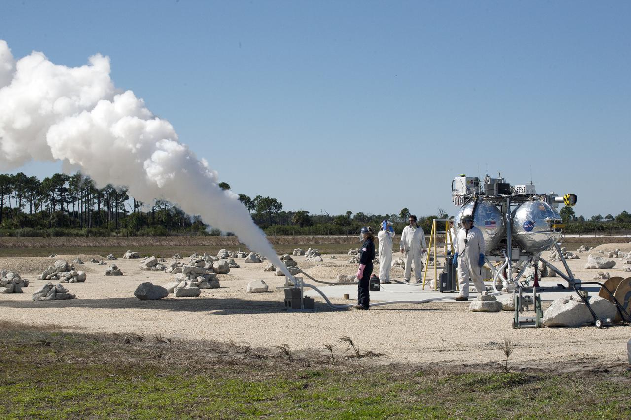 CAPE CANAVERAL, Fla. – Technicians and engineers vent the remaining liquid oxygen from the Project Morpheus prototype lander after it lands on a dedicated pad inside the autonomous landing and hazard avoidance technology, or ALHAT, hazard field at the north end of the Shuttle Landing Facility at NASA’s Kennedy Space Center in Florida. Morpheus launched from the ground over a flame trench on its fifth free flight test at around 1 p.m. EST. It ascended 467 feet, more than 160 feet higher than its last test. Morpheus flew forward, covering 637 feet in 30 seconds before descending on target. Project Morpheus tests NASA’s ALHAT and an engine that runs on liquid oxygen and methane, or green propellants, into a fully-operational lander that could deliver cargo to other planetary surfaces.  The landing facility provides the lander with the kind of field necessary for realistic testing, complete with rocks, craters and hazards to avoid. Morpheus’ ALHAT payload will allow it to navigate to clear landing sites amidst rocks, craters and other hazards during its descent. Project Morpheus is being managed under the Advanced Exploration Systems, or AES, Division in NASA’s Human Exploration and Operations Mission Directorate. The efforts in AES pioneer new approaches for rapidly developing prototype systems, demonstrating key capabilities and validating operational concepts for future human missions beyond Earth orbit. For more information, visit http:__morpheuslander.jsc.nasa.gov. Photo credit: NASA_Kim Shiflett