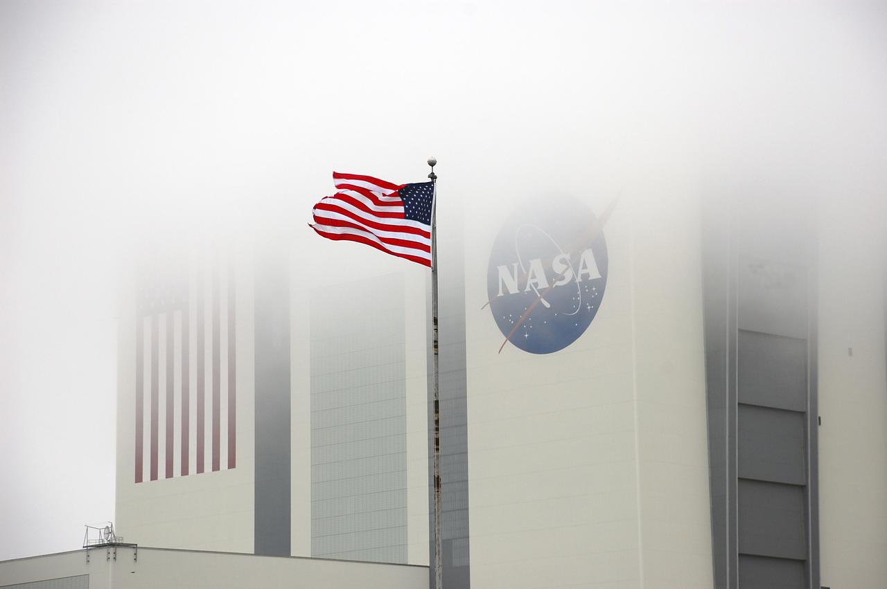 CAPE CANAVERAL, Fla. – At NASA's Kennedy Space Center in Florida, a U.S. flag flies proud near the 525-foot-tall Vehicle Assembly Building, obscured in the fog.  The massive building, once used to process Apollo Saturn V rockets and space shuttles for launch, is undergoing a transformation to prepare it to support NASA's next-generation rocket, the Space Launch System, or SLS, as well as myriad commercial rockets under development. To learn more about the SLS, visit http:__www.nasa.gov_exploration_systems_sls_. For more on NASA's Commercial Crew Program, visit http:__www.nasa.gov_exploration_commercial_crew_. Photo credit: NASA_Ben Smegelsky