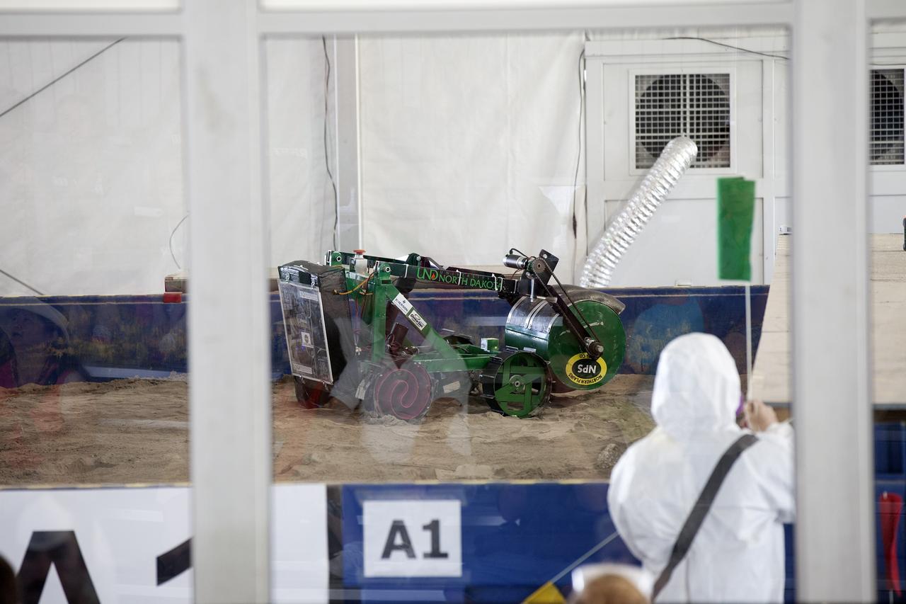 CAPE CANAVERAL, Fla. -- The University of North Dakota's robotic miner digs in the simulated Martian soil in the Caterpillar Mining Arena on the final day of NASA's 2014 Robotic Mining Competition at the Kennedy Space Center Visitor Complex in Florida. More than 35 teams from colleges and universities around the U.S. designed and built remote-controlled robots for the mining competition. The competition is a NASA Human Exploration and Operations Mission Directorate project designed to engage and retain students in science, technology, engineering and mathematics, or STEM, fields by expanding opportunities for student research and design. Teams use their remote-controlled robotics to maneuver and dig in a supersized sandbox filled with a crushed material that has characteristics similar to Martian soil. The objective of the challenge is to see which team’s robot can collect and move the most regolith within a specified amount of time. For more information, visit www.nasa.gov/nasarmc. Photo credit: NASA/Kim Shiflett