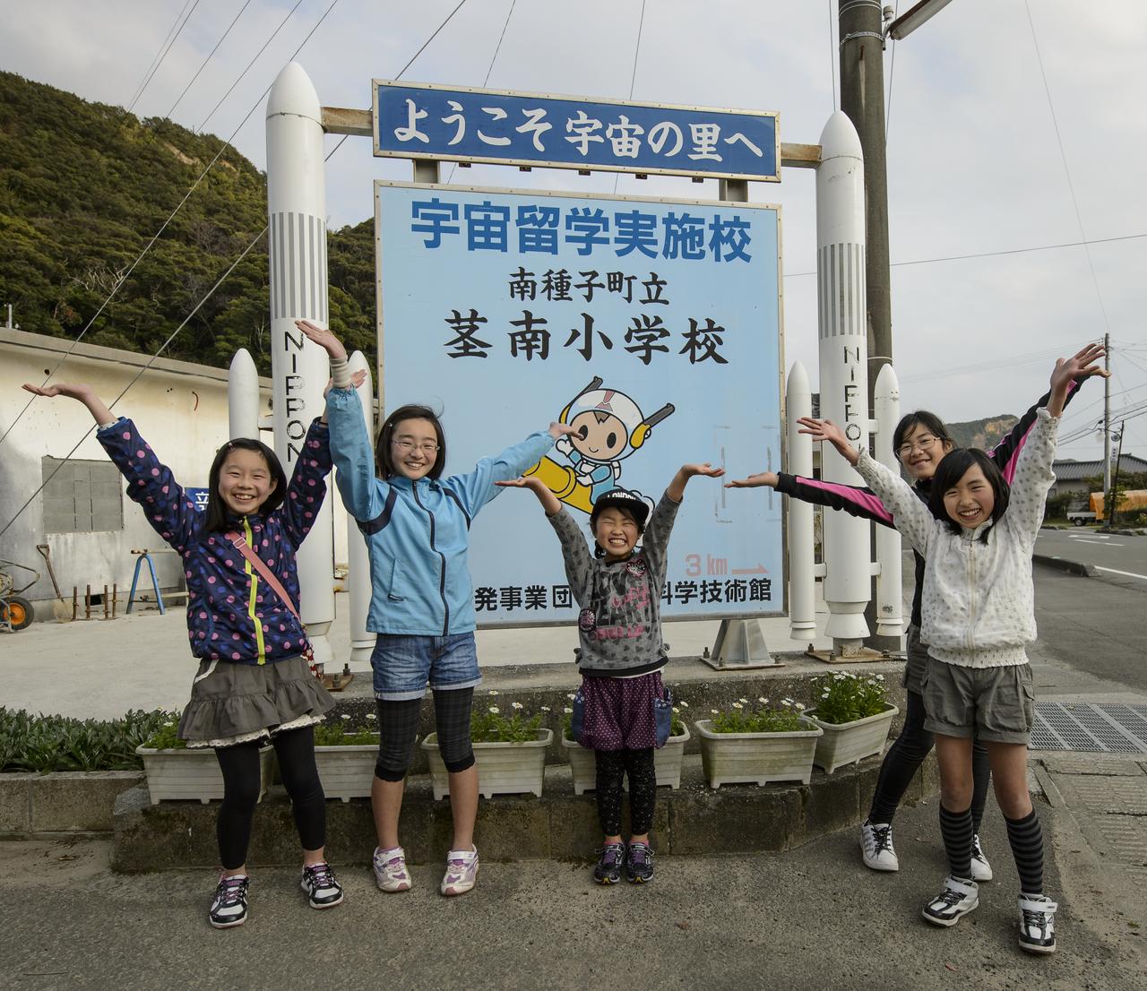 Minamitane elementary school girls pose for a photo in front of a sign featuring the town's mascot "Chuta-kun", Sunday, Feb. 23, 2014, Tanegashima Island, Japan. The Chuta-kun mascot rides a rocket and has guns on the side of his helmet to show the areas history as  the site of the first known contact of Europe and the Japanese, in 1543 and the introduction of the gun. A Japanese H-IIA rocket carrying the NASA-Japan Aerospace Exploration Agency (JAXA), Global Precipitation Measurement (GPM) Core Observatory is planned for launch from the space center on Feb. 28, 2014. Once launched, the GPM spacecraft will collect information that unifies data from an international network of existing and future satellites to map global rainfall and snowfall every three hours.  Photo Credit: (NASA/Bill Ingalls)