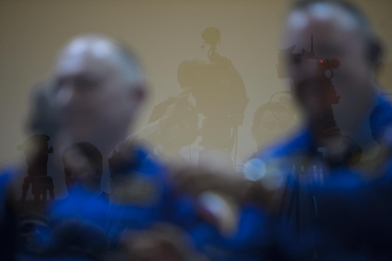 Members of the media are seen reflected in the glass seprating them from the crew of Expedition 39 during the final press conference held ahead of the launch of Expedition 39 prime crew members; Soyuz Commander Alexander Skvortsov of the Russian Federal Space Agency, Flight Engineer Steve Swanson of NASA, and Flight Engineer Oleg Artemyev of Roscosmos, to the International Space Station, Monday, March 24, 2014 at the Cosmonaut Hotel in Baikonur, Kazakhstan. Photo Credit: (NASA/Bill Ingalls)