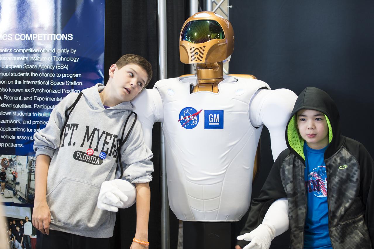Two boys attending the USA Science and Engineering Festival pose with Robonaut 2 at the NASA Stage. Robonaut 2 is NASA's first dexterous humanoid robot that has been working on the International Space Station for the last three years. R2 recently received 1.2 meter long legs to allow mobility. This will enable R2 to assist more with regular and repetitive tasks inside and outside the station. The USA Science and Engineering Festival took place at the Washington Convention Center in Washington, DC on April 26 and 27, 2014. Photo Credit: (NASA/Aubrey Gemignani)
