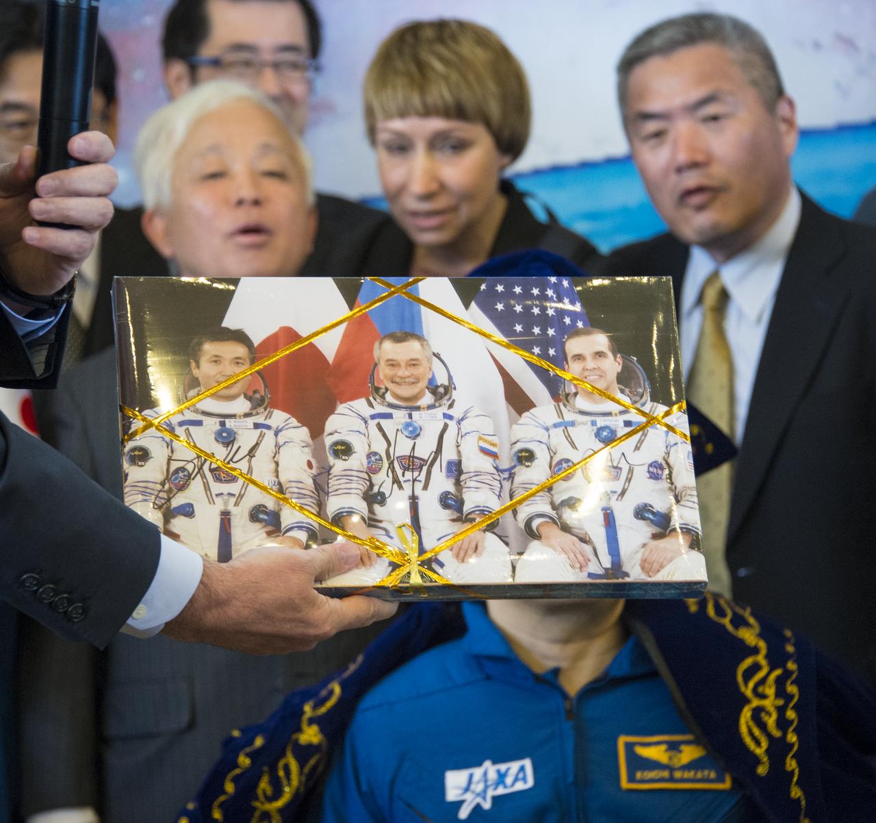 Japan Aerospace Exploration Agency (JAXA) President Naoki Okumura, background left, looks on as a boxes of Karaganda chocolates is presented to Expedition 39 Commander Koichi Wakata of the Japan Aerospace Exploration Agency (JAXA), Soyuz Commander Mikhail Tyurin of Roscosmos, and Flight Engineer Rick Mastracchio of NASA at a welcome ceremony, Wednesday, May 14, 2014 at the Karaganda Airport in Kazakhstan. Wakata, Tyurin and Mastracchio returned to Earth after more than six months onboard the International Space Station where they served as members of the Expedition 38 and 39 crews. Photo Credit: (NASA/Bill Ingalls)