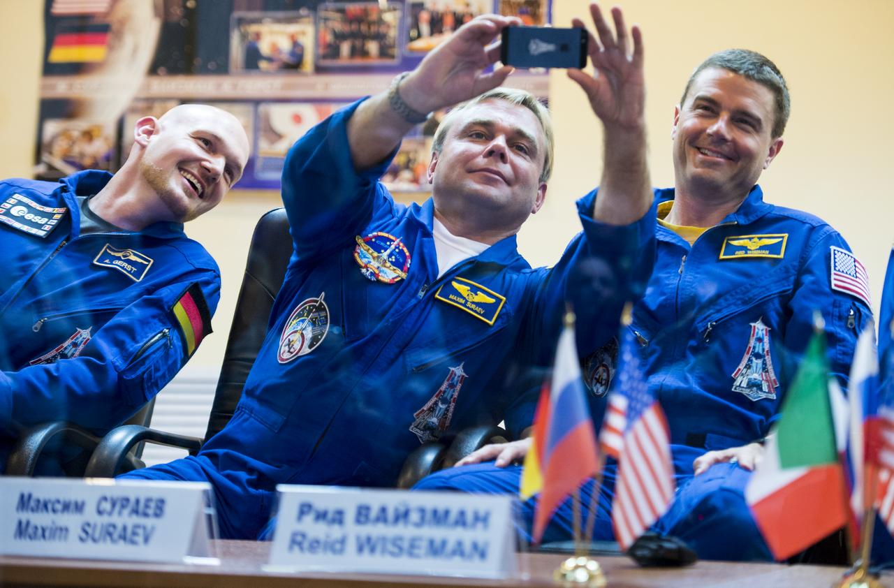 Expedition 40 Soyuz Commander Maxim Suraev of the Russian Federal Space Agency, Roscosmos, center, takes a picture with his cell phone during a press conference, Tuesday, May 27, 2014, at the Cosmonaut Hotel in Baikonur, Kazakhstan. Expedition 40 Soyuz Commander Maxim Suraev of the Russian Federal Space Agency, Roscosmos, Flight Engineer Alexander Gerst of the European Space Agency, ESA, and Flight Engineer Reid Wiseman of NASA will launch aboard their Soyuz TMA-13M spacecraft on their mission to the International Space Station in the early hours of May 29. Photo Credit: (NASA/Joel Kowsky)