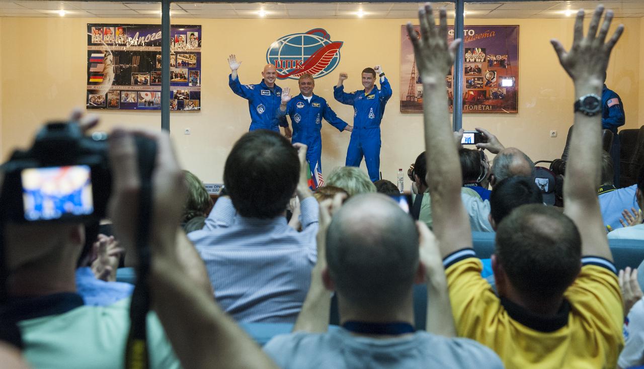 Expedition 40 Flight Engineer Alexander Gerst of the European Space Agency, ESA, left, Soyuz Commander Maxim Suraev of the Russian Federal Space Agency, Roscosmos, center, and Flight Engineer Reid Wiseman of NASA, right, wave to those gathered at the conclusion of a press conference, Tuesday, May 27, 2014, at the Cosmonaut Hotel in Baikonur, Kazakhstan. The mission to the International Space Station is set to launch May 29 from the Baikonur Cosmodrome. Photo Credit: (NASA/Joel Kowsky)