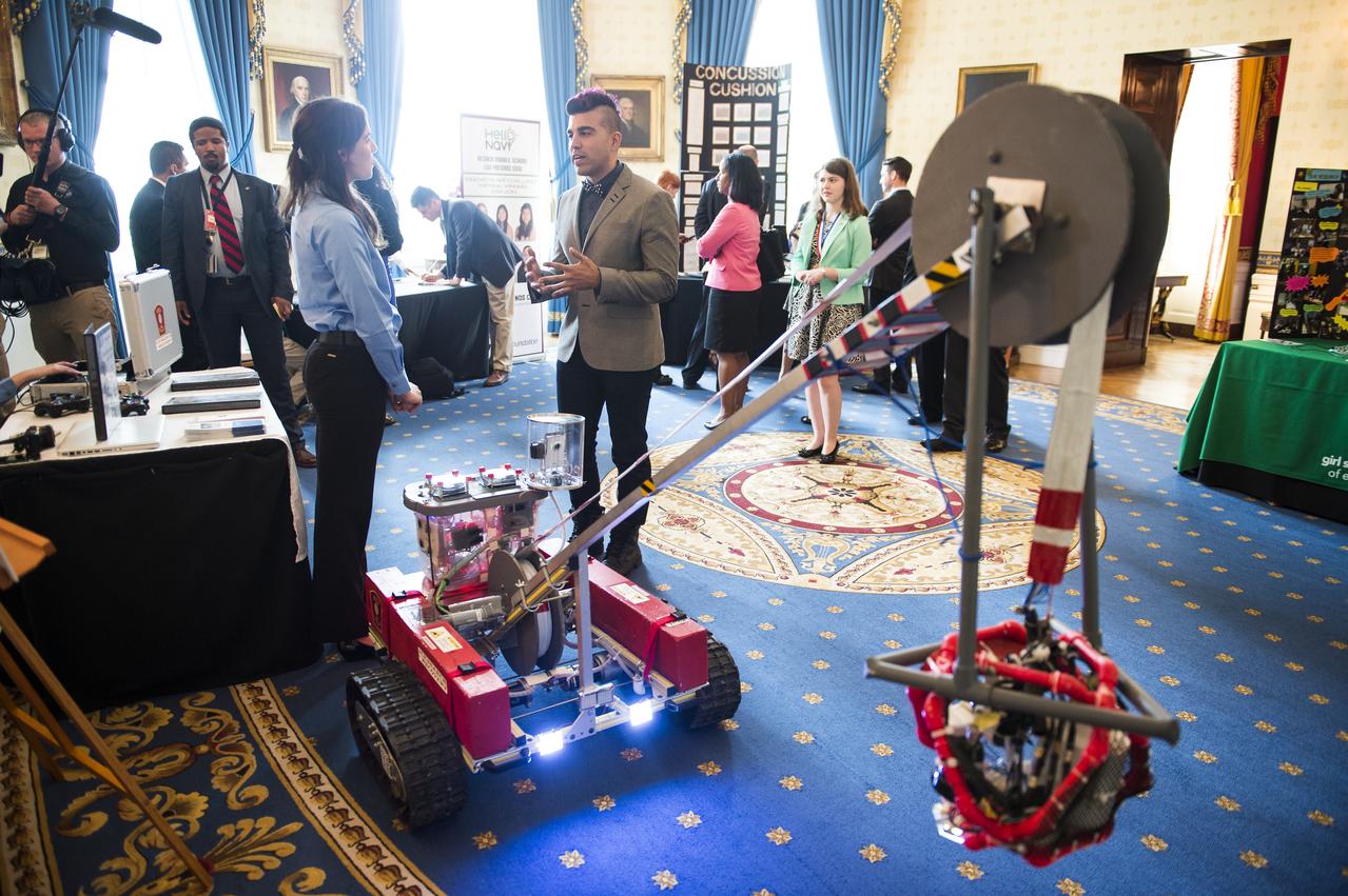 Bobak Ferdowsi, a system's engineer at NASA's Jet Propulsion Laboratory, speaks with a member of "invenTeam" at the White House Science Fair. Olivia Van Amsterdam, 16, Katelyn Sweeney, 17, and their team of student engineers from Natick, MA, invented a 120 lb remotely operated vehicle (ROV) that can help search-and-rescue dive teams search for bodies in dangerous, icy waters. The fourth White House Science Fair was held at the White House and included 100 students from more than 30 different states who competed in science, technology, engineering, and math (STEM) competitions. (Photo Credit: NASA/Aubrey Gemignani)