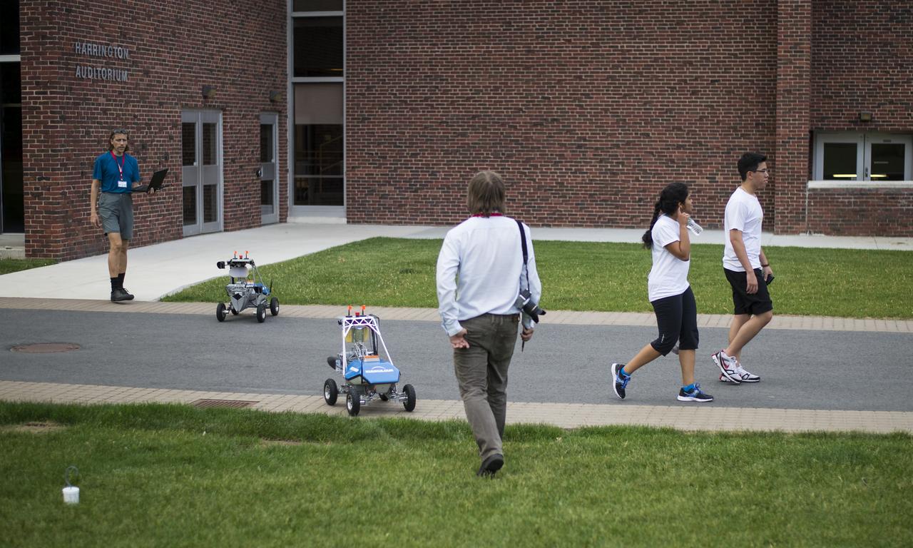 A pair of Worcester Polytechnic Institute (WPI) students walk past a pair of team KuuKulgur's robots on the campus quad, during a final tuneup before the start of competition at the 2014 NASA Centennial Challenges Sample Return Robot Challenge, Tuesday, June 10, 2014, at the Worcester Polytechnic Institute (WPI) in Worcester, Mass.   Team KuuKulgur is one of eighteen teams competing for a $1.5 million NASA prize purse. Teams will be required to demonstrate autonomous robots that can locate and collect samples from a wide and varied terrain, operating without human control. The objective of this NASA-WPI Centennial Challenge is to encourage innovations in autonomous navigation and robotics technologies. Innovations stemming from the challenge may improve NASA's capability to explore a variety of destinations in space, as well as enhance the nation's robotic technology for use in industries and applications on Earth. Photo Credit: (NASA/Joel Kowsky)