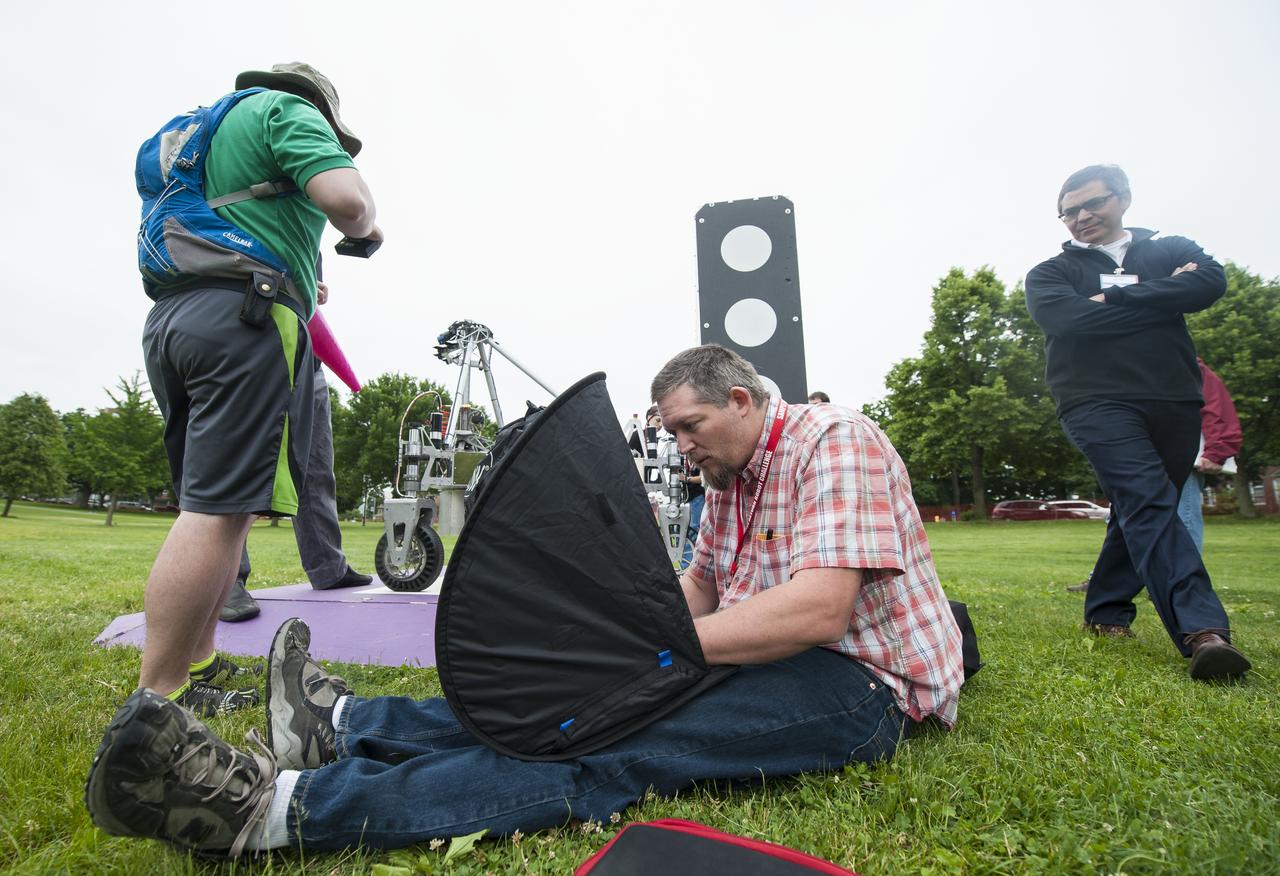 Russel Howe of team Survey, center, works on a laptop to prepare the team's robot for a demonstration run after the team's robot failed to leave the starting platform during it's attempt at the level two challenge at the 2014 NASA Centennial Challenges Sample Return Robot Challenge, Thursday, June 12, 2014, at the Worcester Polytechnic Institute (WPI) in Worcester, Mass.   Eighteen teams are competing for a $1.5 million NASA prize purse. Teams will be required to demonstrate autonomous robots that can locate and collect samples from a wide and varied terrain, operating without human control. The objective of this NASA-WPI Centennial Challenge is to encourage innovations in autonomous navigation and robotics technologies. Innovations stemming from the challenge may improve NASA's capability to explore a variety of destinations in space, as well as enhance the nation's robotic technology for use in industries and applications on Earth. Photo Credit: (NASA/Joel Kowsky)