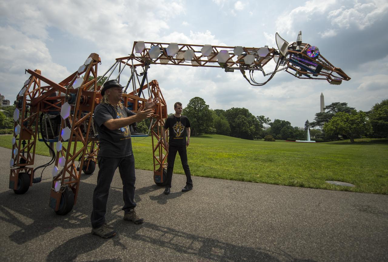 Lindsay Lawlor, of San Diego, Calif., left, demonstrates his creation, a 17-foot-tall, robotic giraffe that "walks" on wheels and is powered by a 12-horsepower hybrid fuel-engine motor, during the first ever White House Maker Faire, which brings together students, entrepreneurs, and everyday citizens who are using new tools and techniques to launch new businesses, learn vital skills in science, technology, engineering, and math (STEM), and fuel the renaissance in American manufacturing, at the White House, Wednesday, June 18, 2014 in Washington. The President announced new steps the Administration and its partners are taking to support the ability of more Americans, young and old, to have to access to these tools and techniques and brings their ideas to life. Photo Credit: (NASA/Bill Ingalls)