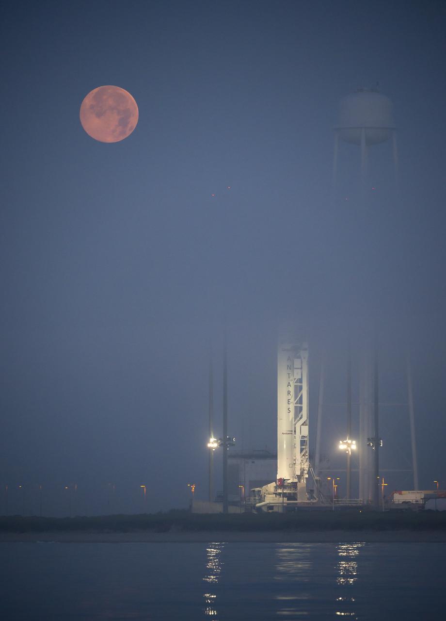 The full Moon sets in the fog behind the Orbital Sciences Corporation Antares rocket, with the Cygnus spacecraft onboard, Saturday, July 12, 2014, launch Pad-0A, NASA's Wallops Flight Facility in Virginia. The Antares will launch with the Cygnus spacecraft filled with over 3,000 pounds of supplies for the International Space Station, including science experiments, experiment hardware, spare parts, and crew provisions. The Orbital-2 mission is Orbital Sciences' second contracted cargo delivery flight to the space station for NASA. Photo Credit: (NASA/Bill Ingalls)