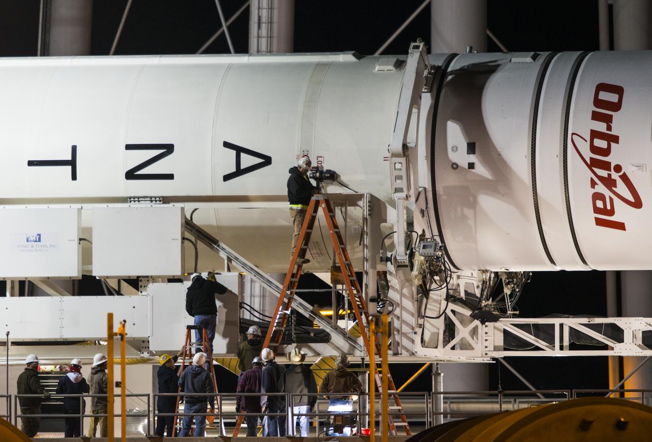 Workers are seen as they prepare the Orbital Sciences Corporation Antares rocket, with the Cygnus spacecraft onboard, to be raised at launch Pad-0A, Friday, Oct. 24, 2014, at NASA's Wallops Flight Facility in Virginia. The Antares will launch with the Cygnus spacecraft filled with over 5,000 pounds of supplies for the International Space Station, including science experiments, experiment hardware, spare parts, and crew provisions. The Orbital-3 mission is Orbital Sciences' third contracted cargo delivery flight to the space station for NASA. Photo Credit: (NASA/Joel Kowsky)