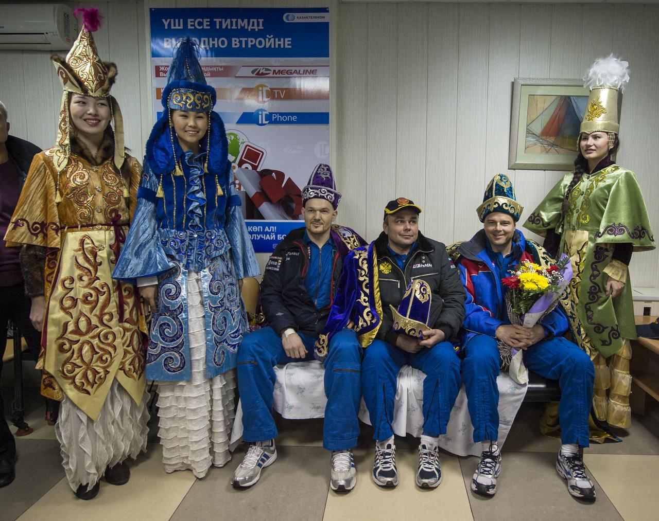 Expedition 41 light Engineer Alexander Gerst of the European Space Agency (ESA), seated left, Commander Max Suraev of the Russian Federal Space Agency (Roscosmos), center, and NASA Flight Engineer Reid Wiseman, pose for a photograph with women in kazakh ceremonial dress during a welcome ceremony at the Kustanay Airport shortly after they arrived there via helicopter from their Soyuz landing site in a remote area near the town of Arkalyk, Kazakhstan on Monday, Nov. 10, 2014. Suraev, Wiseman and Gerst returned to Earth after more than five months onboard the International Space Station where they served as members of the Expedition 40 and 41 crews. Photo Credit: (NASA/Bill Ingalls)