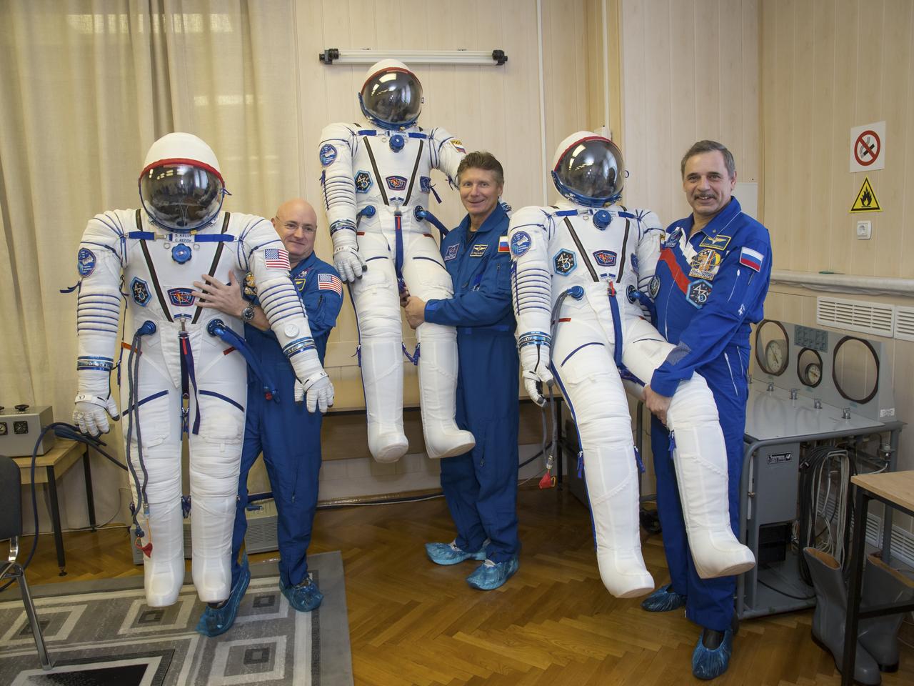 Expedition 43 NASA Astronaut Scott Kelly, left, and Russian Cosmonauts Gennady Padalka, center, and Mikhail Kornienko of the Russian Federal Space Agency (Roscosmos) take a moment during their Soyuz TMA-16M spacecraft fit check to pose for a photograph while holding their pressurized Russian Sokol suits, Sunday, March 15, 2015 at the Baikonur Cosmodrome in Kazakhstan. The trio are preparing for launch to the International Space Station in their Soyuz TMA-16M spacecraft from the Baikonur Cosmodrome in Kazakhstan March 28, Kazakh time. As the one-year crew, Kelly and Kornienko will return to Earth on Soyuz TMA-18M in March 2016. Photo Credit: (NASA/Victor Zelentsov)