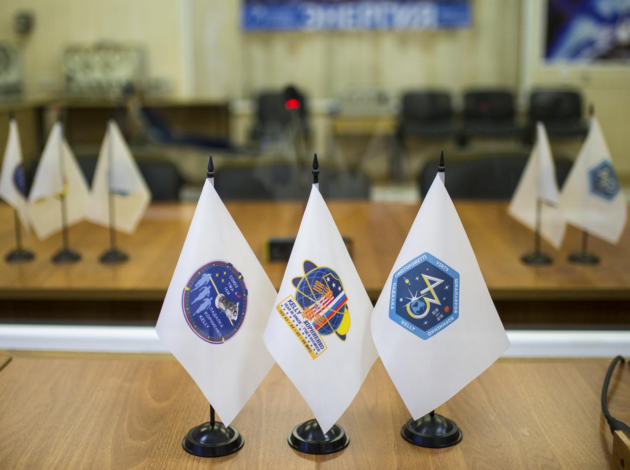 Flags depicting the Soyuz TMA-16M spacecraft, the One-Year Mission, and the Expedition 43 Mission are seen on desks in two different rooms separated by glass where Expedition 43 prime and backup crews will meet with space officials on their final check of the Soyuz capsule, Monday, March 23, 2015 at the Baikonur Cosmodrome in Kazakhstan. NASA Astronaut Scott Kelly, and Russian Cosmonauts Mikhail Kornienko, and Gennady Padalka of the Russian Federal Space Agency (Roscosmos) are scheduled to launch to the International Space Station in the Soyuz TMA-16M spacecraft from the Baikonur Cosmodrome in Kazakhstan March 28, Kazakh time (March 27 Eastern time.) As the one-year crew, Kelly and Kornienko will return to Earth on Soyuz TMA-18M in March 2016. Photo Credit: (NASA/Bill Ingalls)