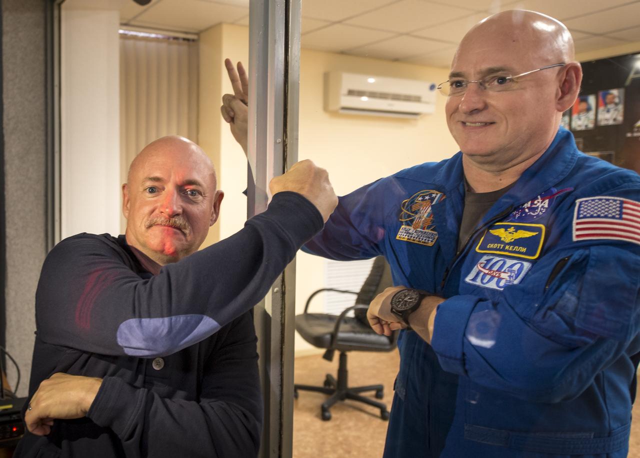 Retired NASA Astronaut Mark Kelly, left, fist pumps his identical twin brother, NASA Astronaut Scott Kelly through glass as Scott Kelly and fellow crew mates, Russian cosmonauts Gennady Padalka, and Mikhail Kornienko of the Russian Federal Space Agency (Roscosmos) participate in a press conference while in quarantine Thursday, March 26, 2015, at the Cosmonaut Hotel in Baikonur, Kazakhstan. Mark Kelly, who flew four space shuttle missions and commanded the final flight of space shuttle Endeavour, will participate in biomedical studies on the ground while his twin is on board the orbiting laboratory. Scott Kelly, Kornienko, and Padalka launched to the International Space Station in the Soyuz TMA-16M spacecraft from the Baikonur Cosmodrome in Kazakhstan March 28, Kazakh time (March 27 Eastern time.) As the one-year crew, Kelly and Kornienko will return to Earth on Soyuz TMA-18M in March 2016.  Photo Credit (NASA/Bill Ingalls)