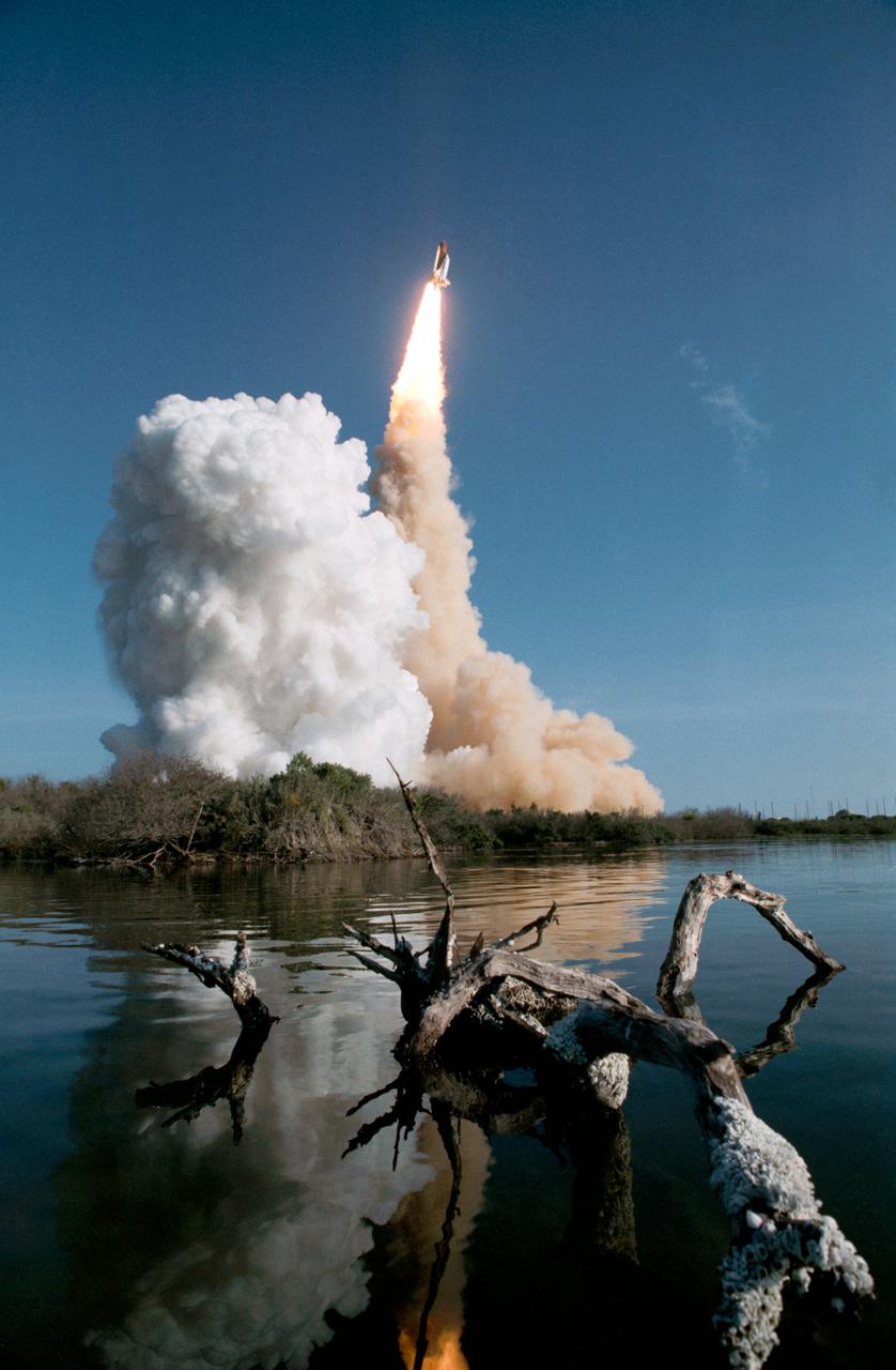 View of the launch of the shuttle Discovery and the 41-D mission. The orbiter and its plume of smoke are photographed from across the river in the early stages of liftoff (3085,3087); The orbiter can be seen just clearing the pad, with a cloud of smoke billowing to the left of the frame. The orbiters two orbital maneuvering system (OMS) pods and external tank are visible along with the orbiter (3086).