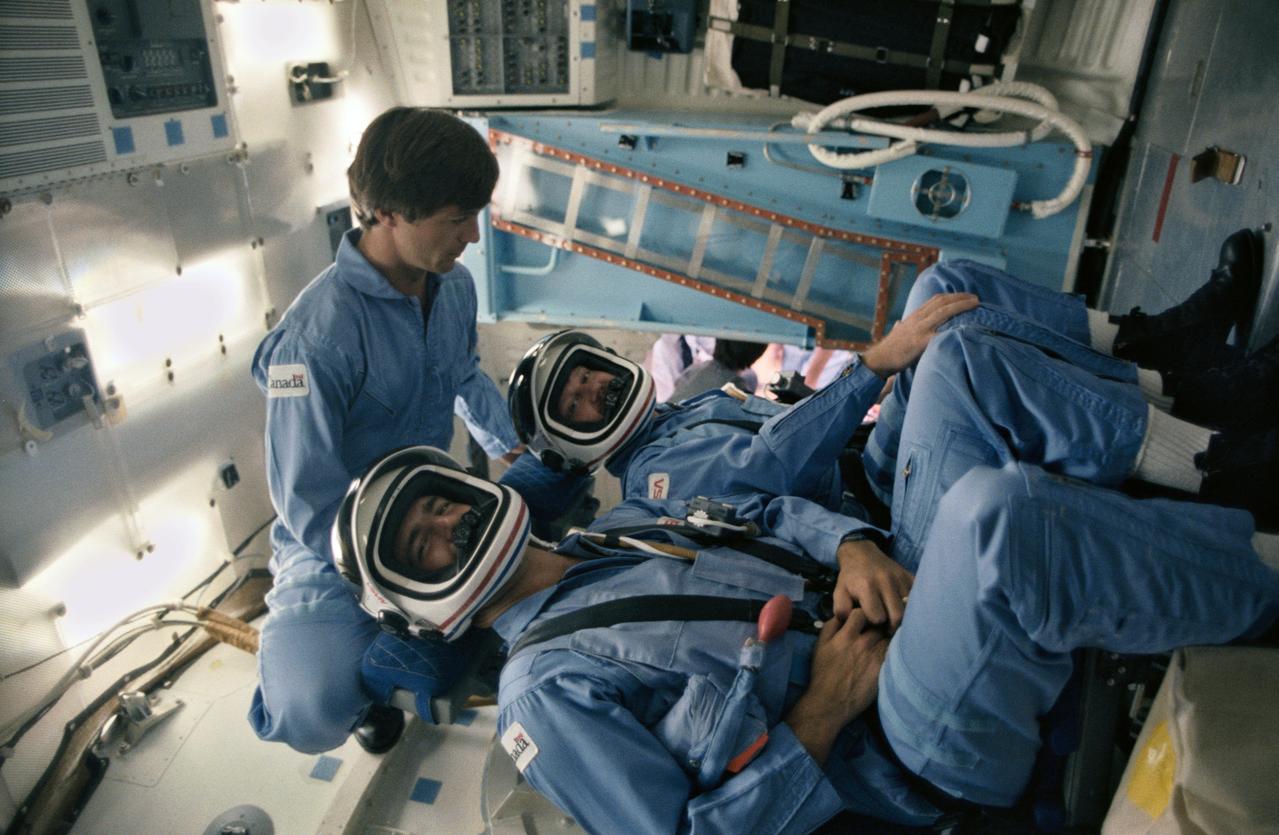 41D-3138 (4 Sept 1984)--- Canada's backup payload specialist assists the two 41-G prime payload specialists during a training session in the Johnson Space Center's Shuttle mockup and integration laboratory.  Robert Thirsk (without helmet) represents the National Research Council (NRC) and is backup to Marc Garneau (nearest camera), also of the NRC.  Paul D. Scully-Power, seated in the other middeck seat for the launch phase, is a civilian oceanographer with the U.S. Navy.  The 41-G flight aboard the Challenger is NASA's first to utilize a crew of more than six persons.  This photograph was taken by Otis Imboden.