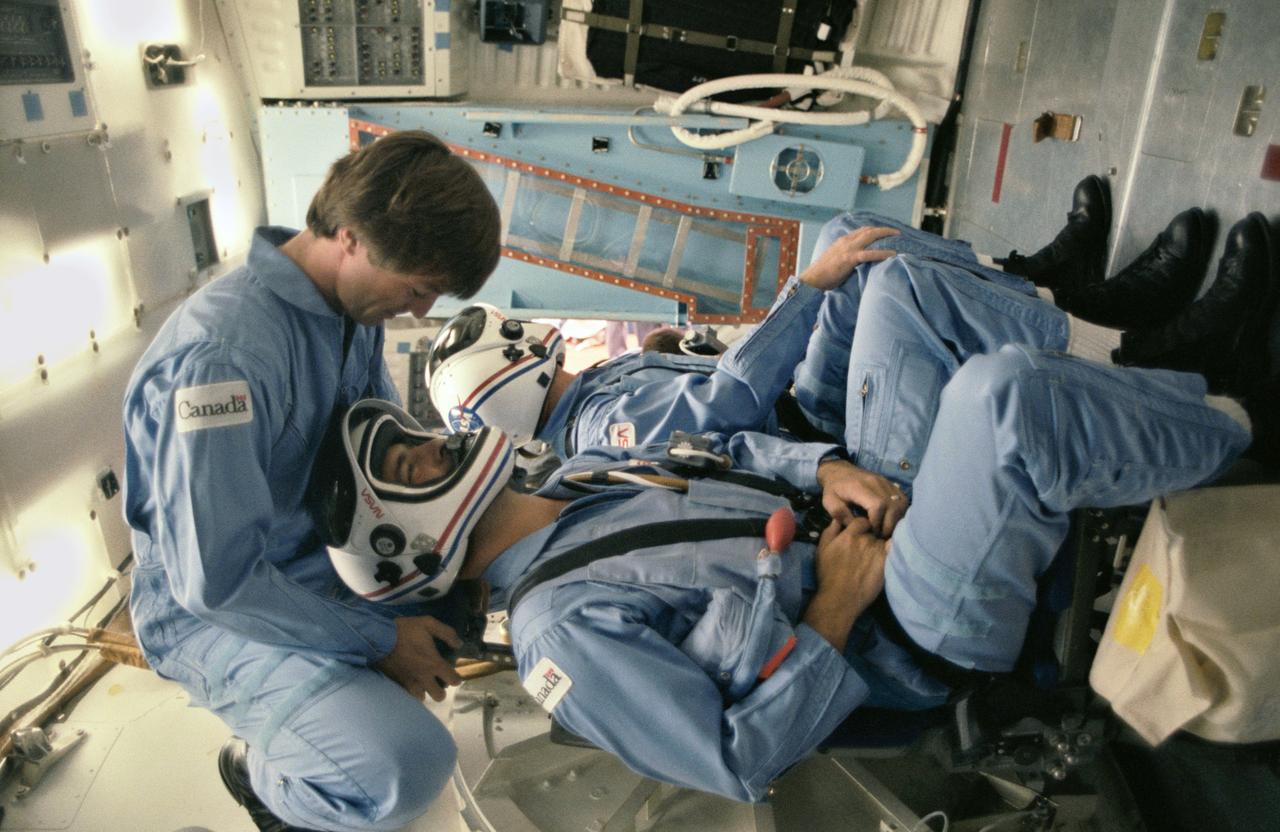 41D-3139 (2 Sept 1984) --- Two prime crew member payload specialist and a backup for NASA's 41-G Space Shuttle mission participate in launch phase simulations at the Johnson Space Center. Securing themselves in temporary stations in the middeck of a trainer are Marc Garneau,  representing the Canadian National Research Council (NRC), and Paul D.  Scully-Power (background), a U.S. Navy oceanographer.  Robert Thirsk, also with  the NRC, is a backup payload specialist.  This photograph was taken by Otis Imboden.