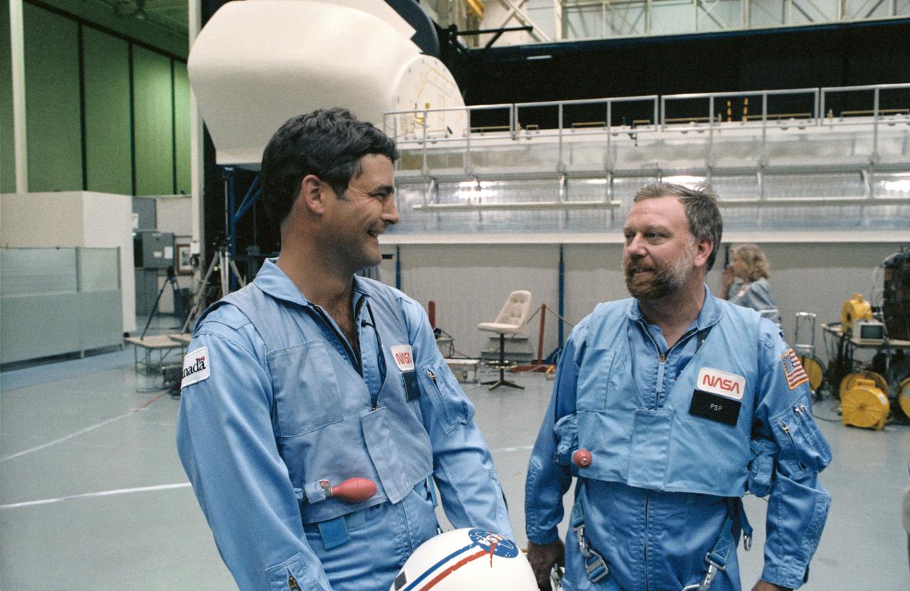 41D-3185 (S14-3185) (4 Sept 1984) --- The two payload specialists for NASA's 41-G mission aboard the Challenger chat prior to a simulation session in the Shuttle mockup and integration laboratory at the Johnson Space Center.  They are Marc Garneau, left,   representing the Canadian National Research   Council, and Paul D. Scully-Power, an   oceanographer with the U.S. Navy.  They are   standing near the manipulator development facility (MDF), pictured in background.