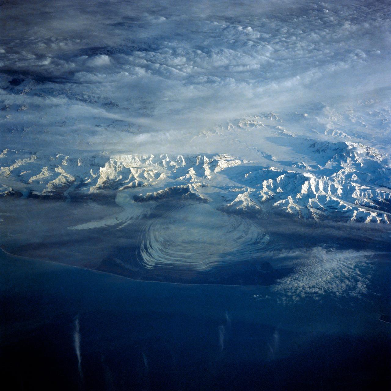 41G-43-016 (5-13 Oct 1984) --- The Gulf of Alaska, with the great peaks of the Saint Elias Range of Alaska, Yukon, and British Columbia. Mount Logan, Canada's highest mountain peak at 19,850 feet, is to the left of the center of the photograph. Between Saint Elias Peak and Mount Vancouver, right of center, flows the great Malaspina Glacier in a great lobe of ice shaped like a human ear.