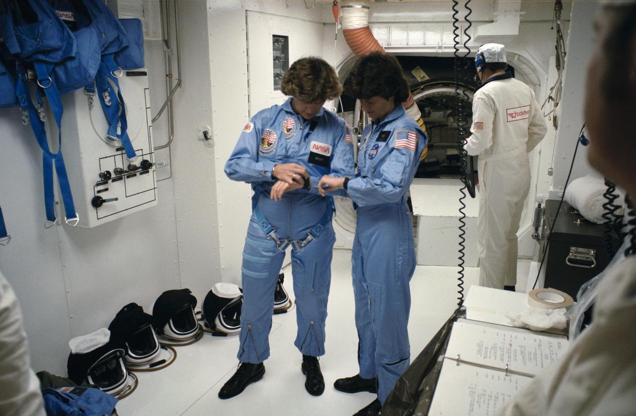 41G-90082 / S17-90082 (5 Oct 1984) --- Astronauts Sally K. Ride (right) and Kathryn D. Sullivan, two of three mission specialists, synchronize their watches prior to ingressing the Space Shuttle Challenger on the launch pad at Kennedy Space Center (KSC).  They are in the White Room leading to the entry hatch of the vertically configured spacecraft.
