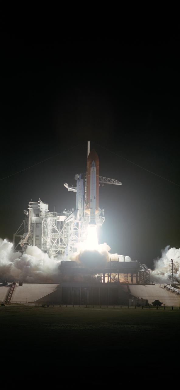 View of the early morning launch of STS 41-G Challenger. The dark launch complex is illuminated by spotlights as the orbiter begins its ascent from the pad.