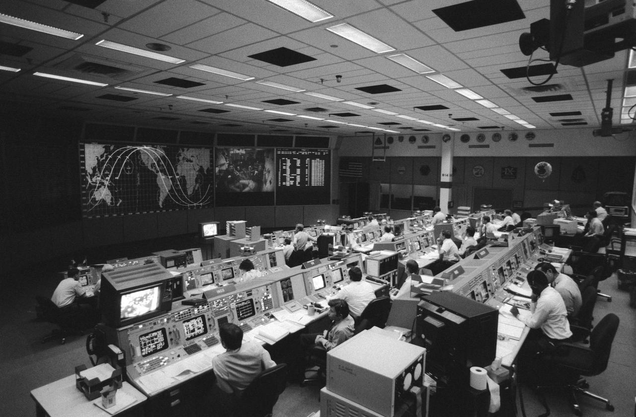 Wide angle view of the flight control room (FCR) of the Mission Control Center (MCC). Some of the STS 41-G crew can be seen on a large screen at the front of the MCC along with a map tracking the progress of the orbiter.