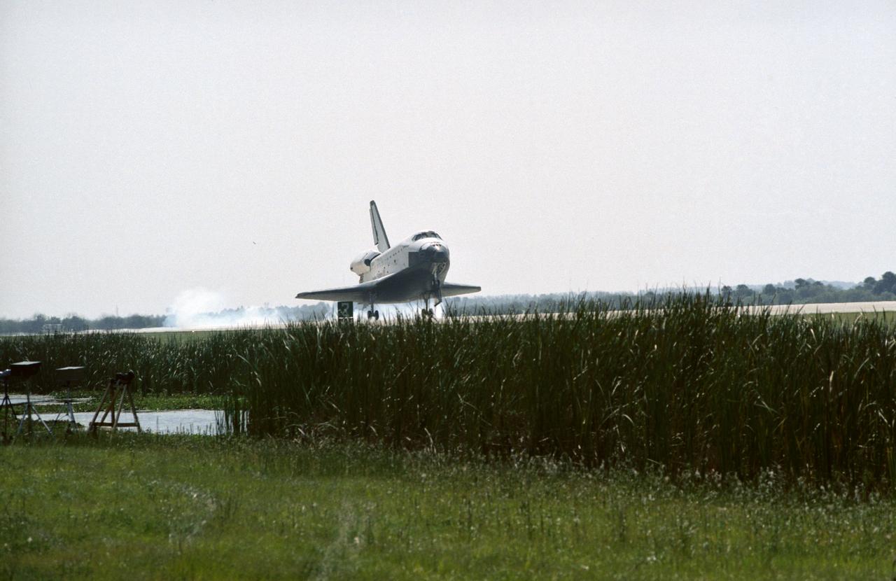 The Space Shuttle Challenger lands at Kennedy Space Center (KSC) at the end of the STS 41-G mission. The main landing gear has already touched down in this view, but the nose gear is still in the air (90232); Front view through tall grass of the Challenger making its landing at KSC (90233); Close-up side view of the Challenger making its landing at KSC (90234); Aerial view of the Challenger making its final approach to the runway to land at KSC (90235).