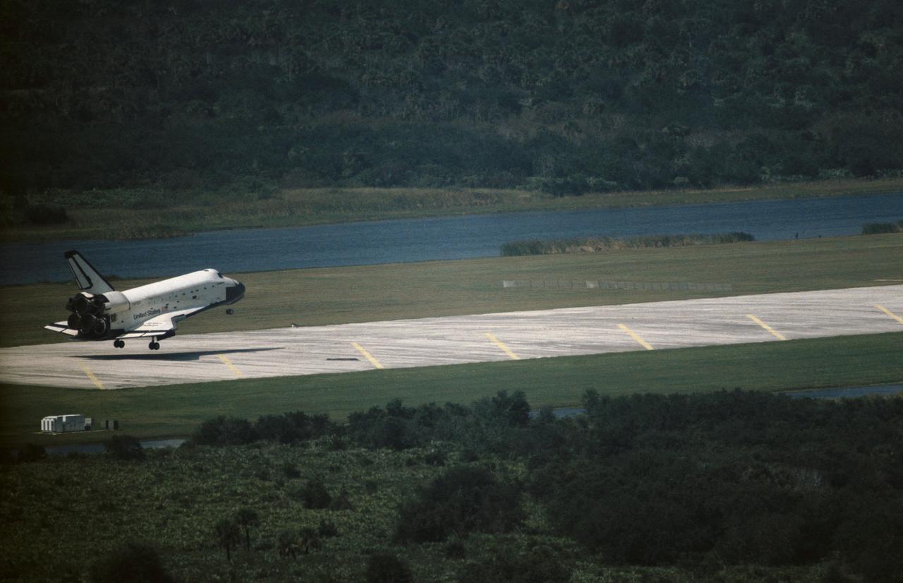 The Space Shuttle Challenger lands at Kennedy Space Center (KSC) at the end of the STS 41-G mission. The main landing gear has already touched down in this view, but the nose gear is still in the air (90232); Front view through tall grass of the Challenger making its landing at KSC (90233); Close-up side view of the Challenger making its landing at KSC (90234); Aerial view of the Challenger making its final approach to the runway to land at KSC (90235).