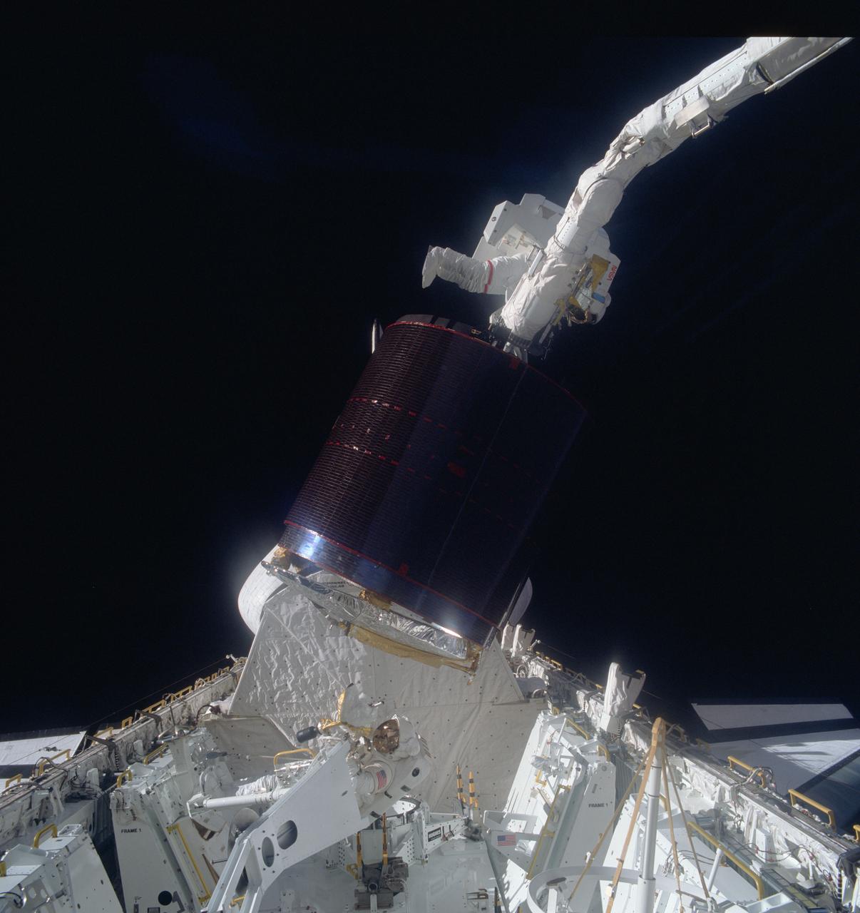 51A-41-021 (12 Nov 1984) --- Astronaut Joseph P. Allen IV, top, hangs onto a stinger device, which earlier had stabilized the pictured Palapa B-2 communications satellite, as astronaut Dale A. Gardner in the cargo bay of Discovery waits to assist in the berthing of the previously stranded spinning spacecraft.  The end effector of the remote manipulatore system (RMS), controlled from inside Discovery's cabin by astronaut Anna L. Fisher, grasps a special grapple point to Allen's right.  A fellow crewmember on the flight deck, using a 70mm handheld Hasselblad camera, exposed the frame.  The activity took place on November 12, 1984.